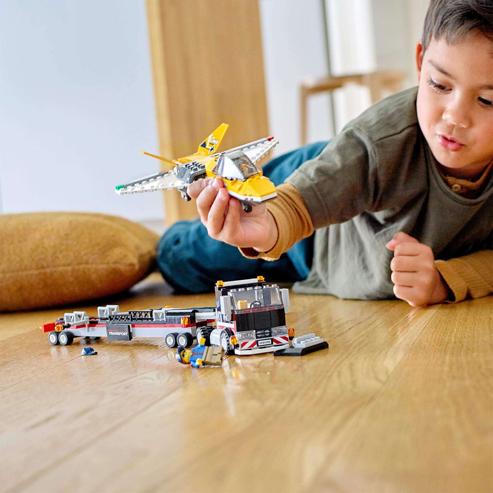 Child playing with LEGO® City Airshow Jet Transporter Toy 60289, featuring a jet and transporter on a wooden floor.