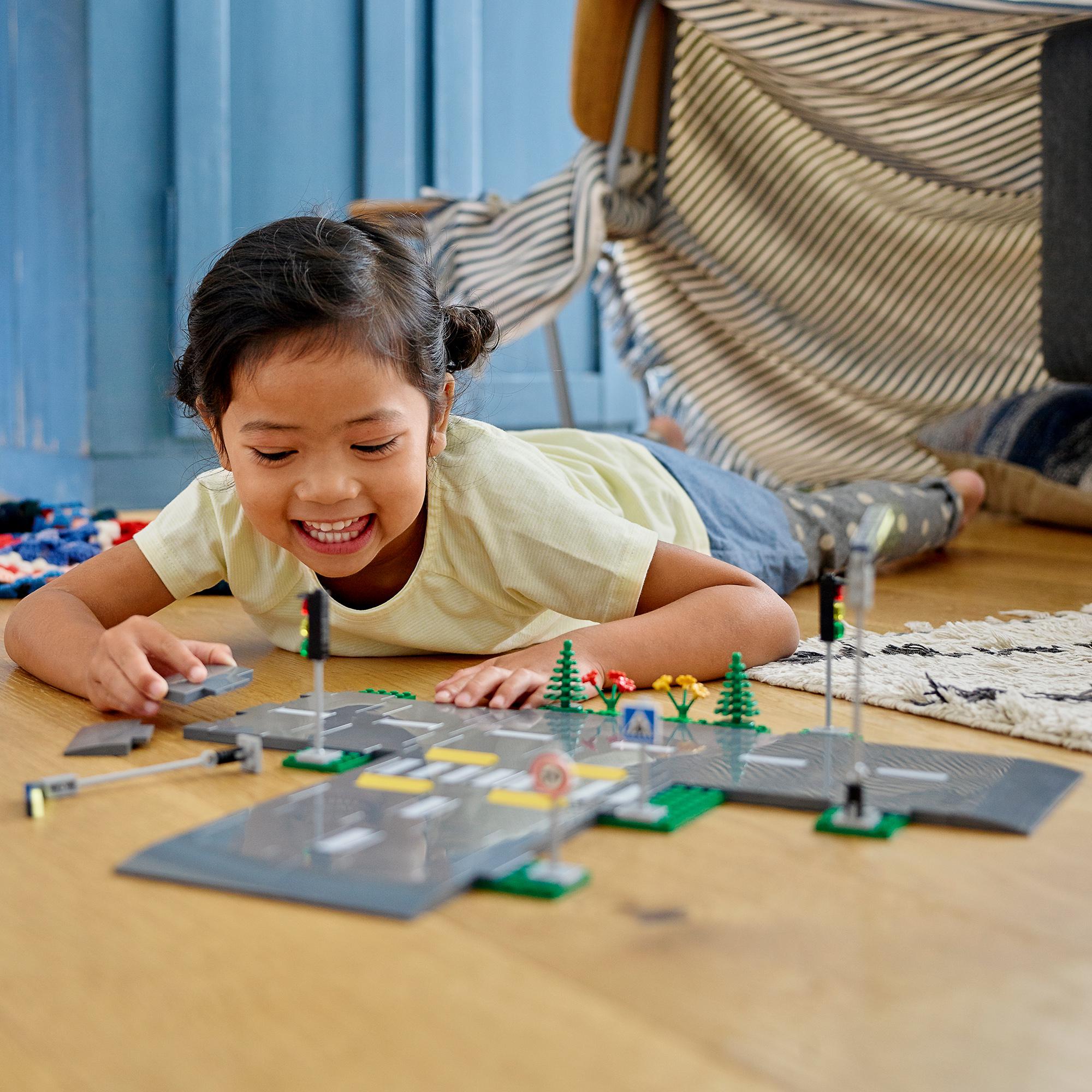 Child playing with LEGO® City Road Plates set, featuring streetlights, traffic signs, and a pedestrian crossing.