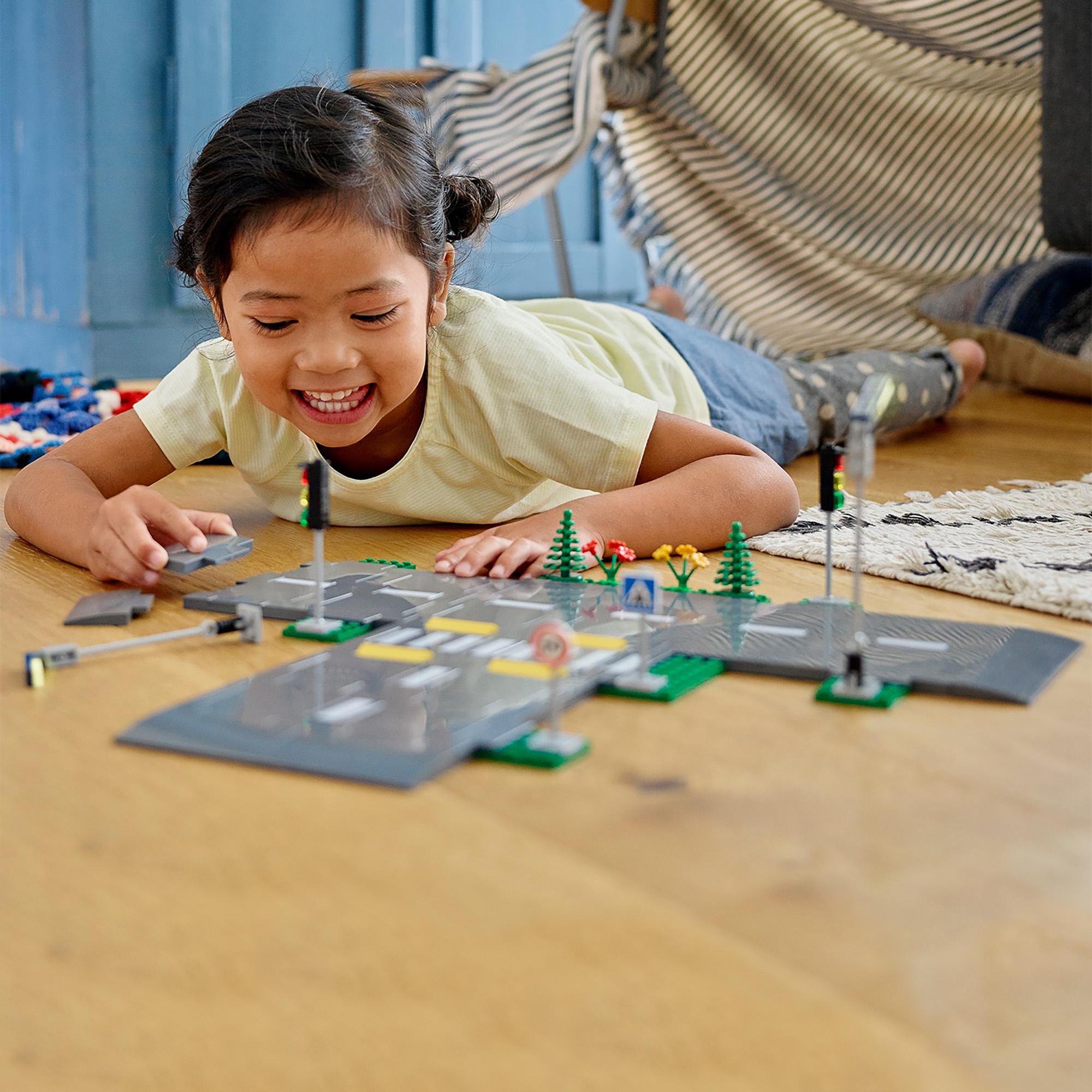 Child playing with LEGO® City Road Plates set featuring road signs, traffic lights, and streetlights on the floor.