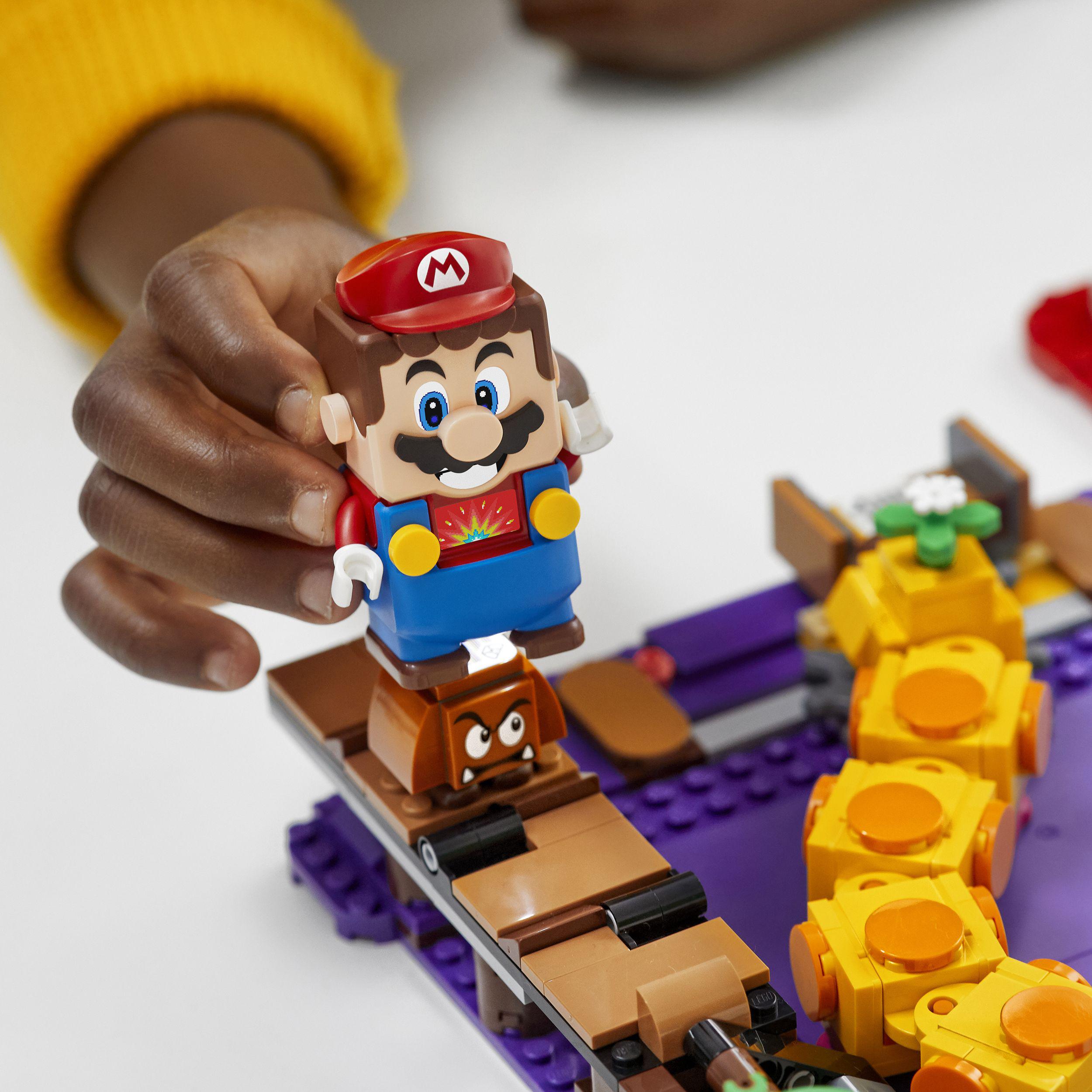 Child plays with LEGO® Super Mario figure atop a Goomba in the Poison Swamp Expansion Set 71383 building scene.