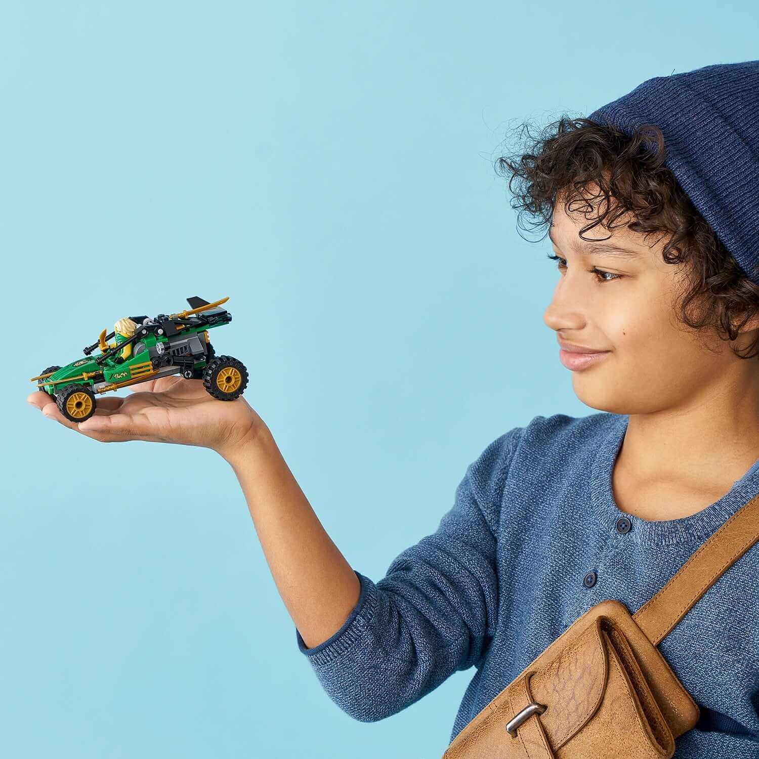 Child holding LEGO® NINJAGO Legacy Jungle Raider Set 71700, showcasing creativity and play in a vibrant setting.