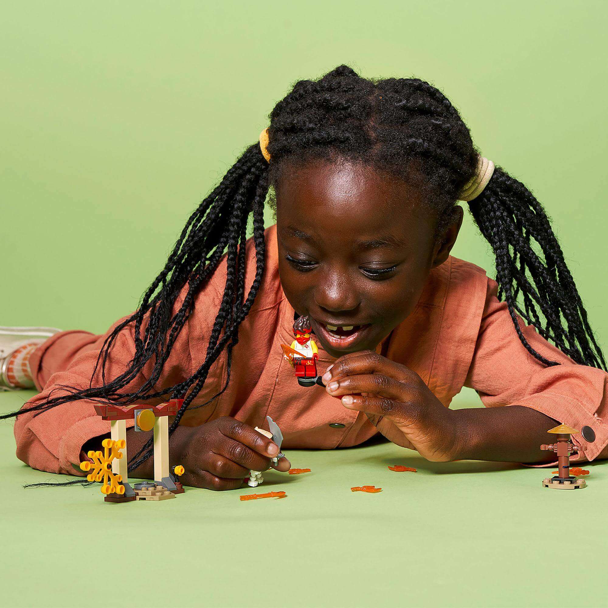 Child playing with LEGO® NINJAGO Epic Battle Set, featuring Kai and Skulkin, on a green background.