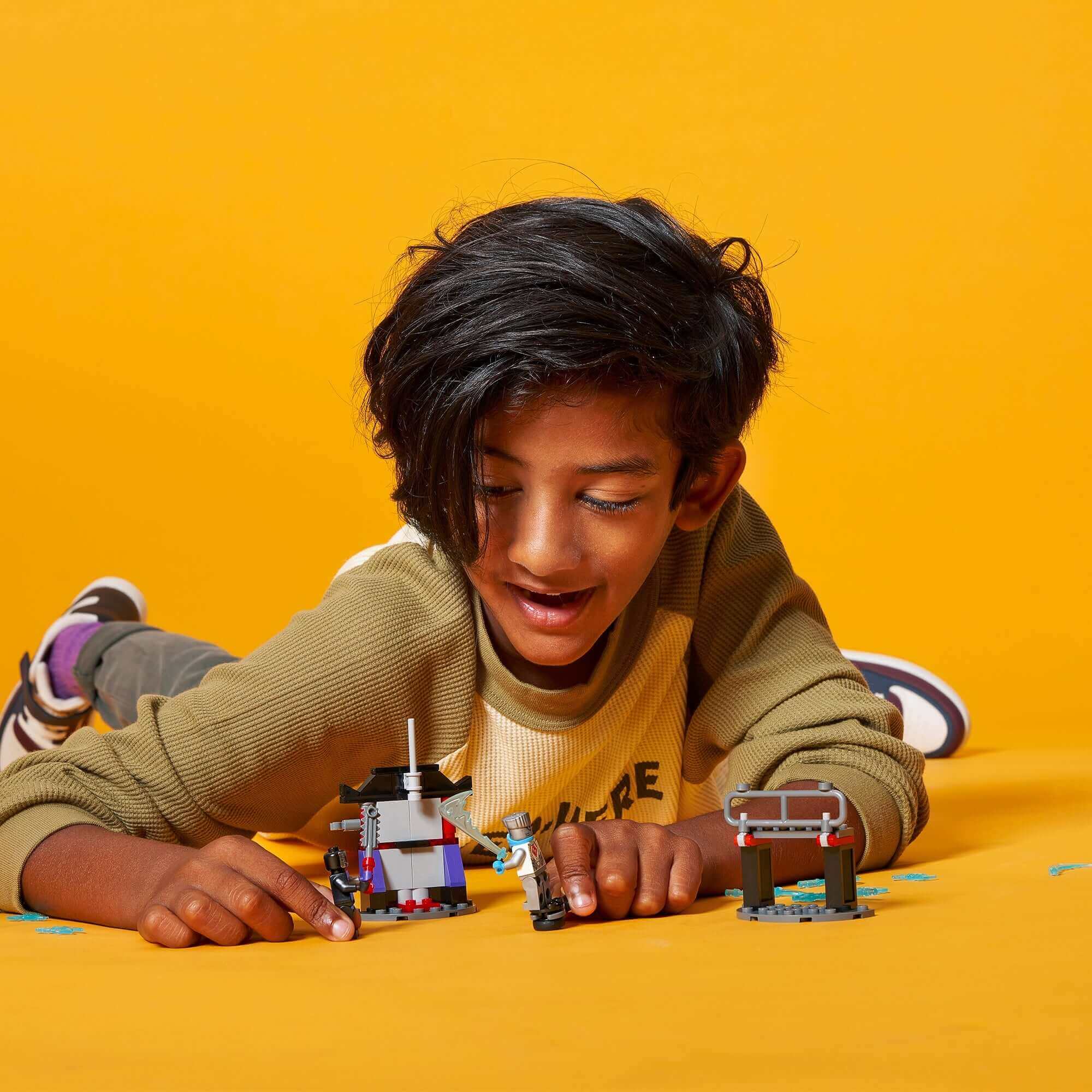 Child playing with LEGO® NINJAGO Epic Battle Set Zane vs. Nindroid on a bright yellow background.