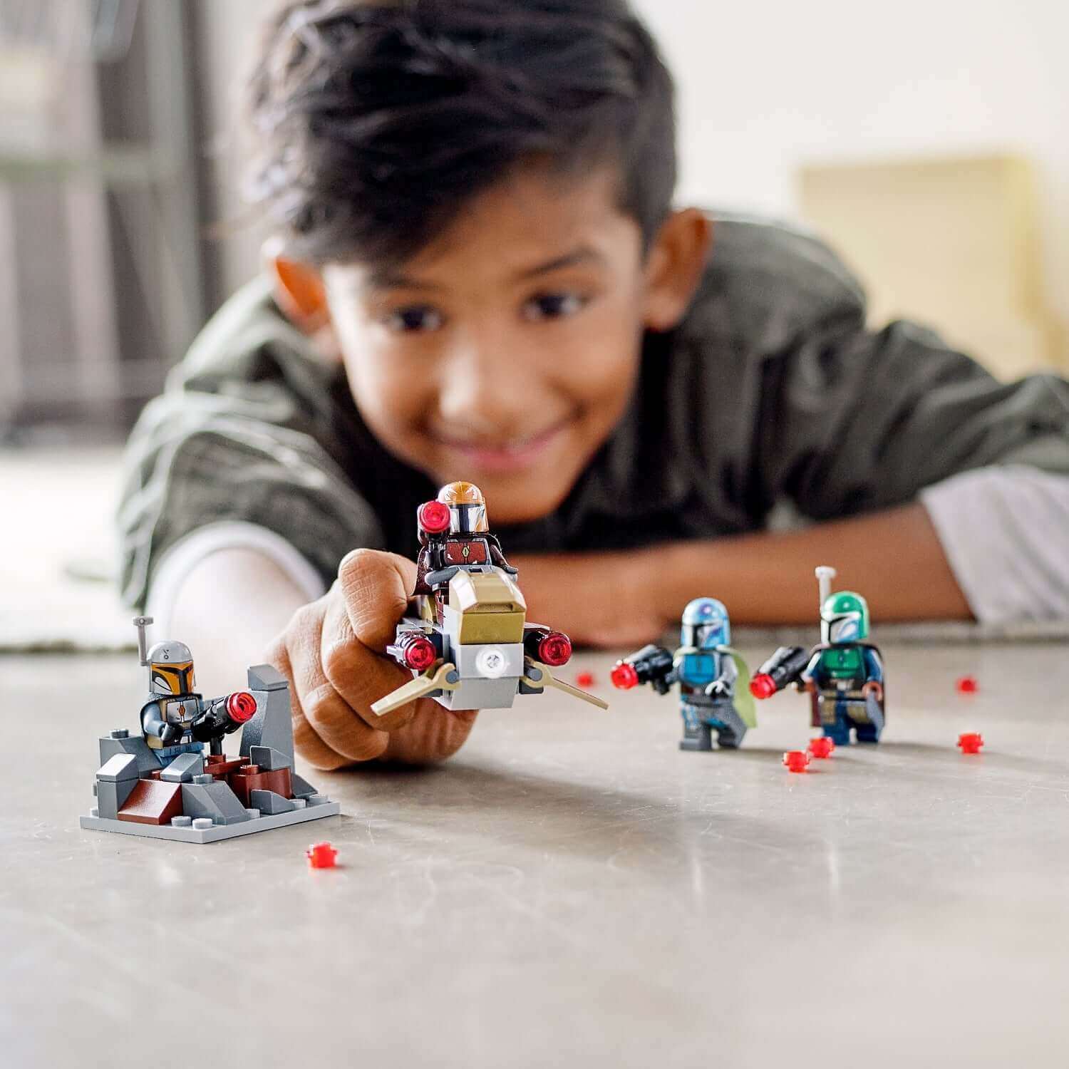 Child playing with LEGO® Star Wars Mandalorian Battle Pack set 75267, featuring minifigures, speeder, and defense fort.