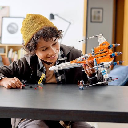 Child playing with LEGO Star Wars Poe Dameron's X-wing Fighter 75273 on a table, engaging in imaginative play.