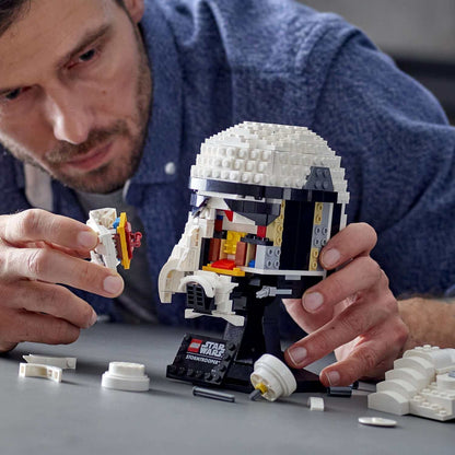 Adult builder assembling LEGO Star Wars Stormtrooper Helmet Model Set 75276 with intricate details on display.