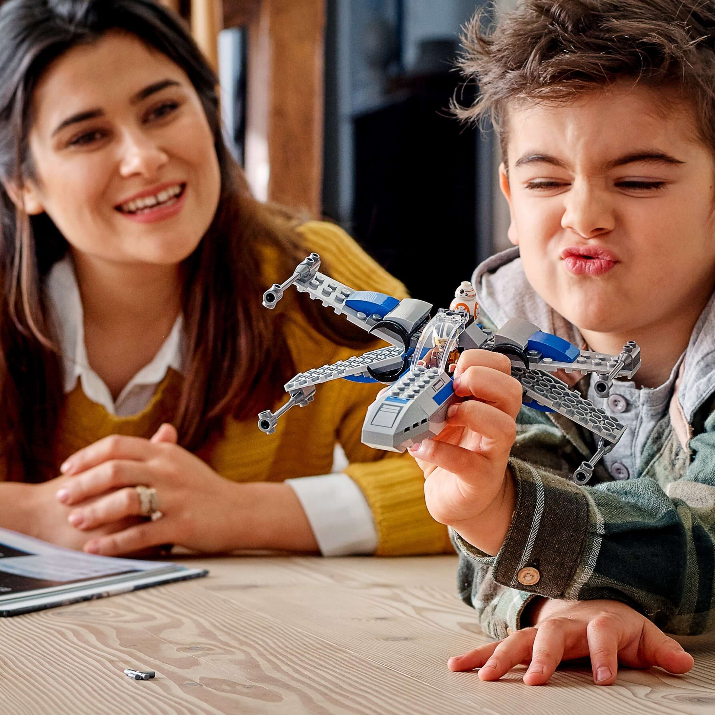 Child playing with LEGO® Star Wars Resistance X-wing set, smiling with excitement while adult watches.