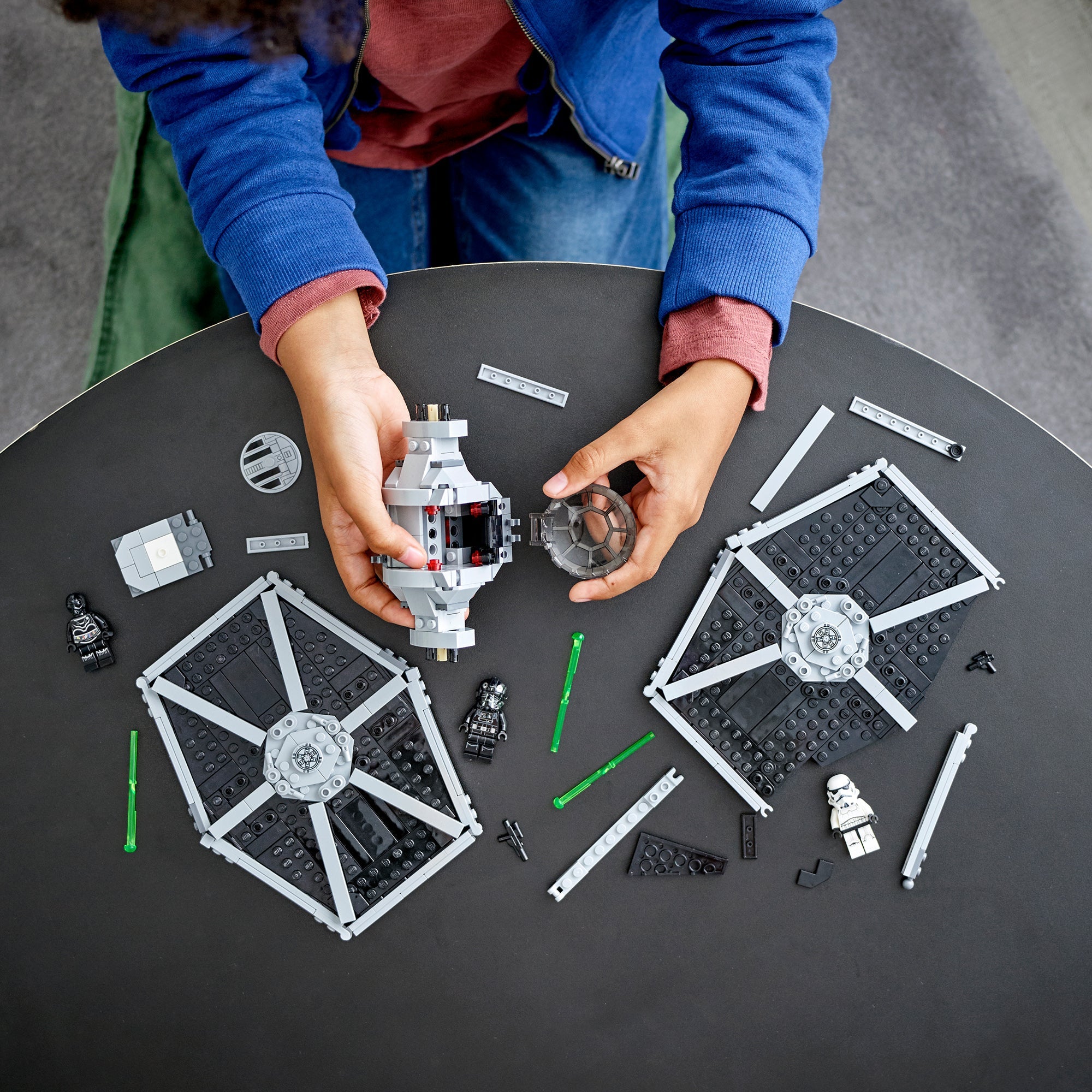 Child assembling LEGO® Star Wars Imperial TIE Fighter set 75300 with minifigures and building pieces on a table.