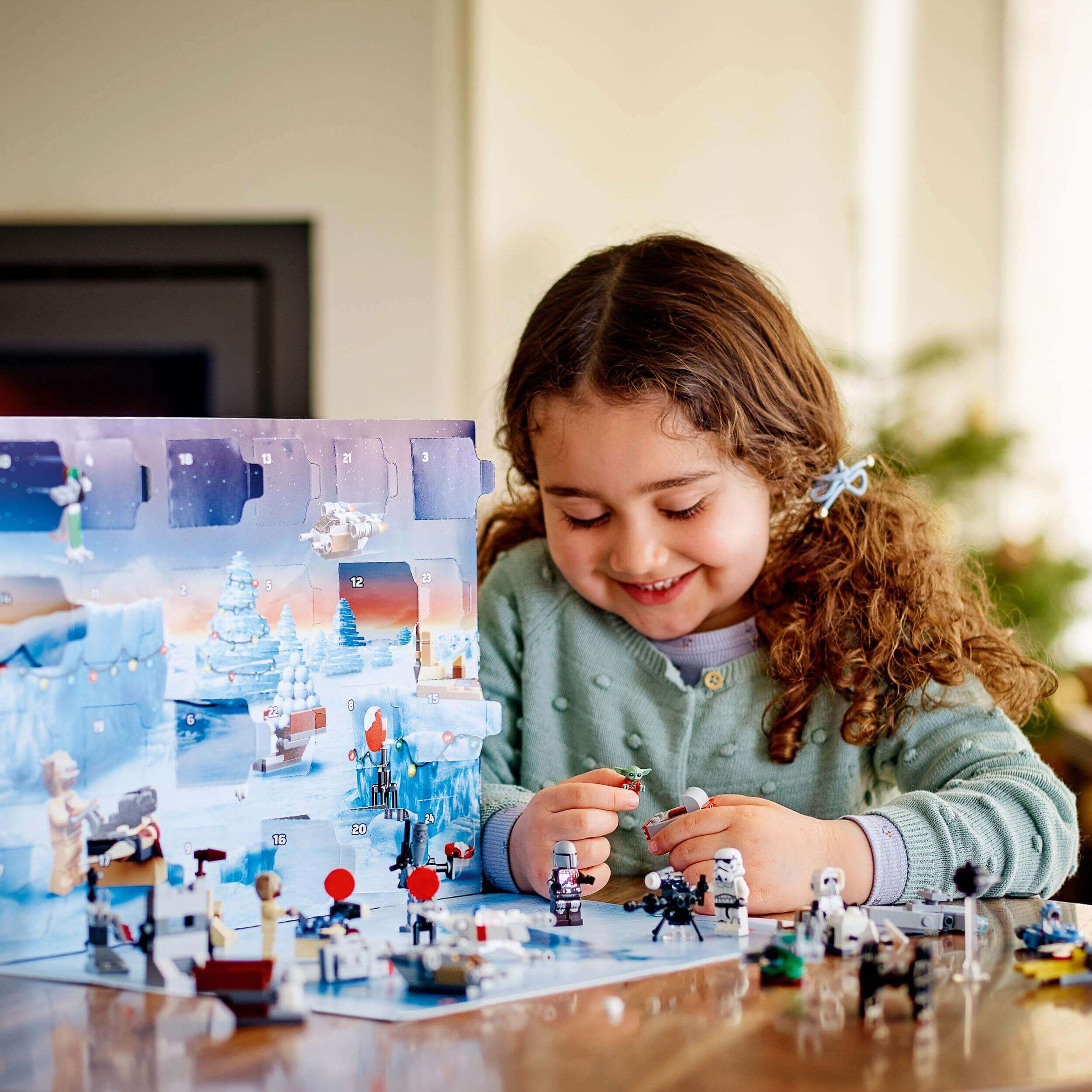 Child joyfully playing with LEGO Star Wars Advent Calendar, unveiling Mandalorian buildable toys and festive elements.
