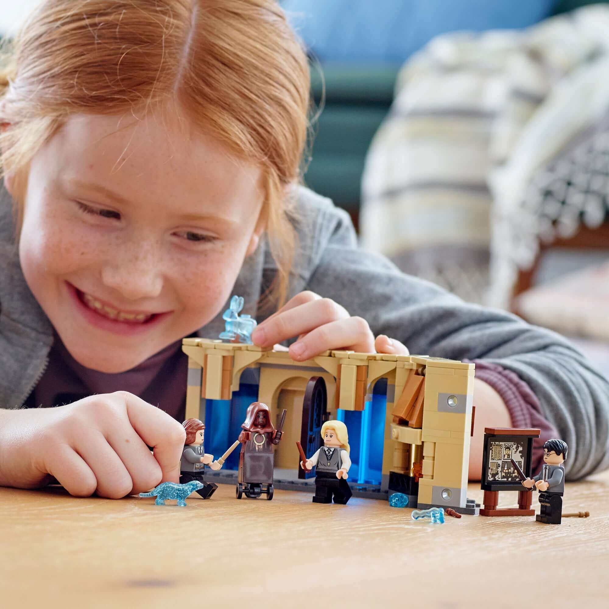 Child playing with LEGO Harry Potter Room of Requirement set, featuring Harry, Hermione, and Luna in a magical scene.