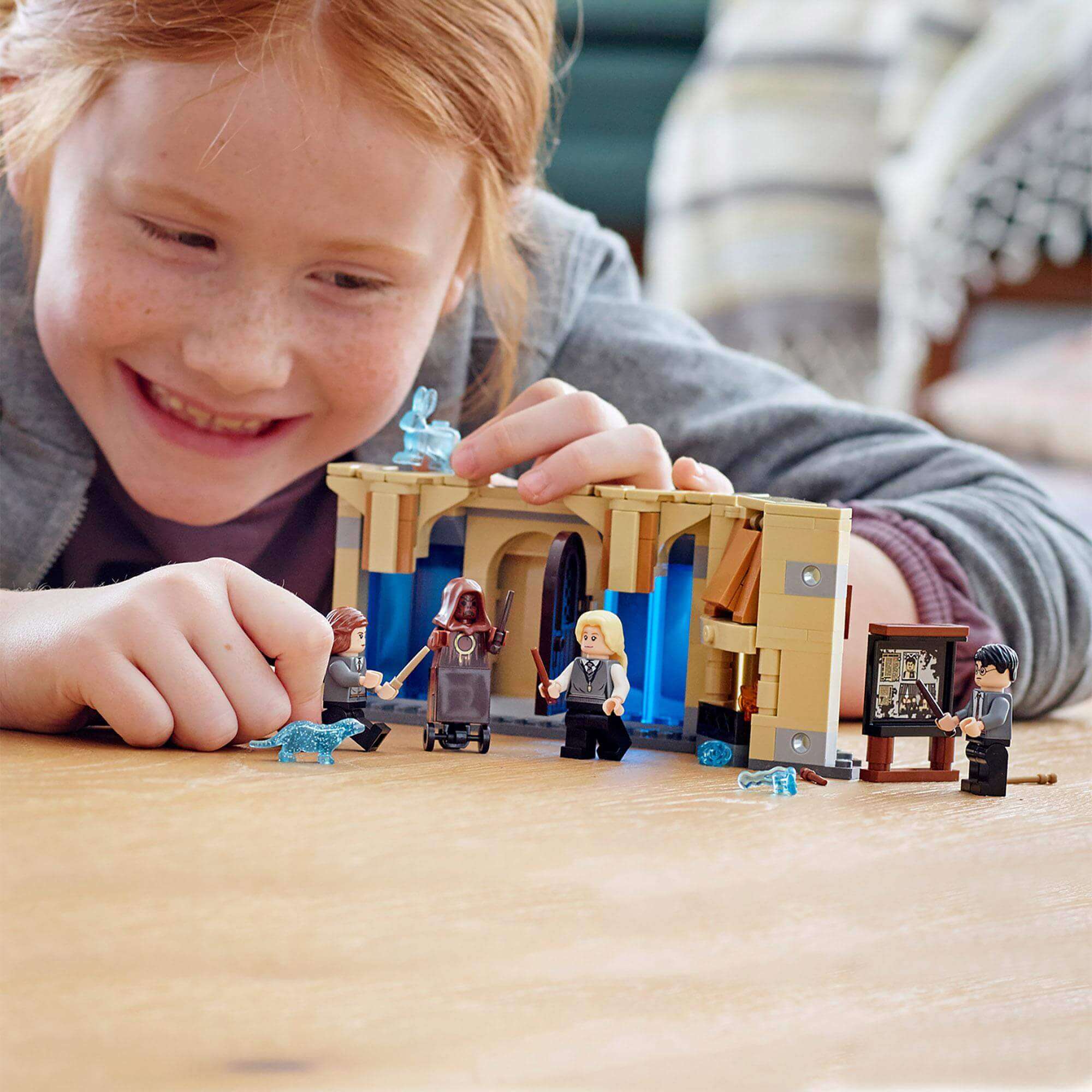 Child enjoying LEGO® Harry Potter Room of Requirement set with figures of Harry, Hermione, and Luna.