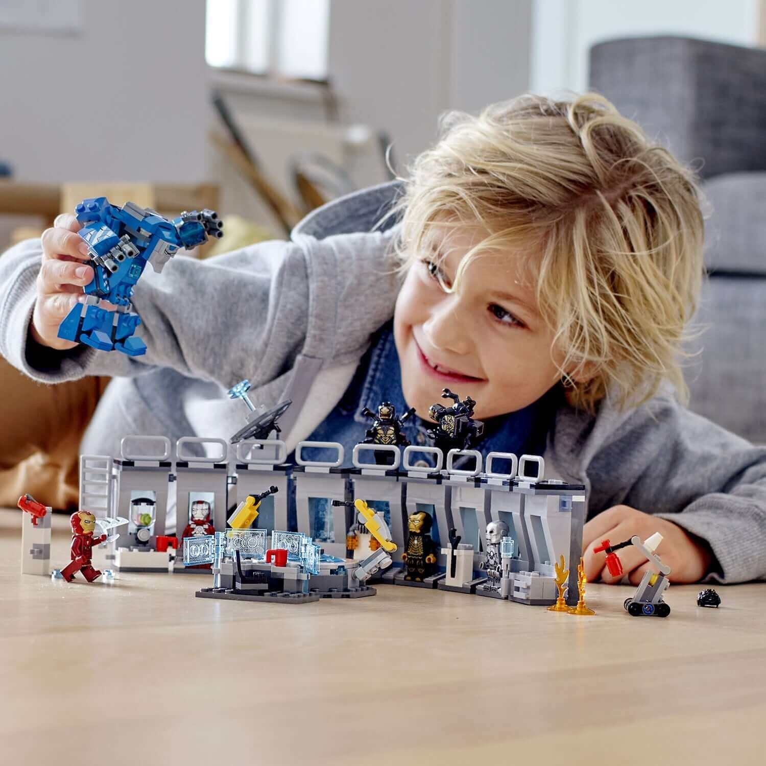 Child playing with LEGO Marvel Avengers Iron Man Hall of Armor 76125 set, featuring Iron Man suits and accessories.