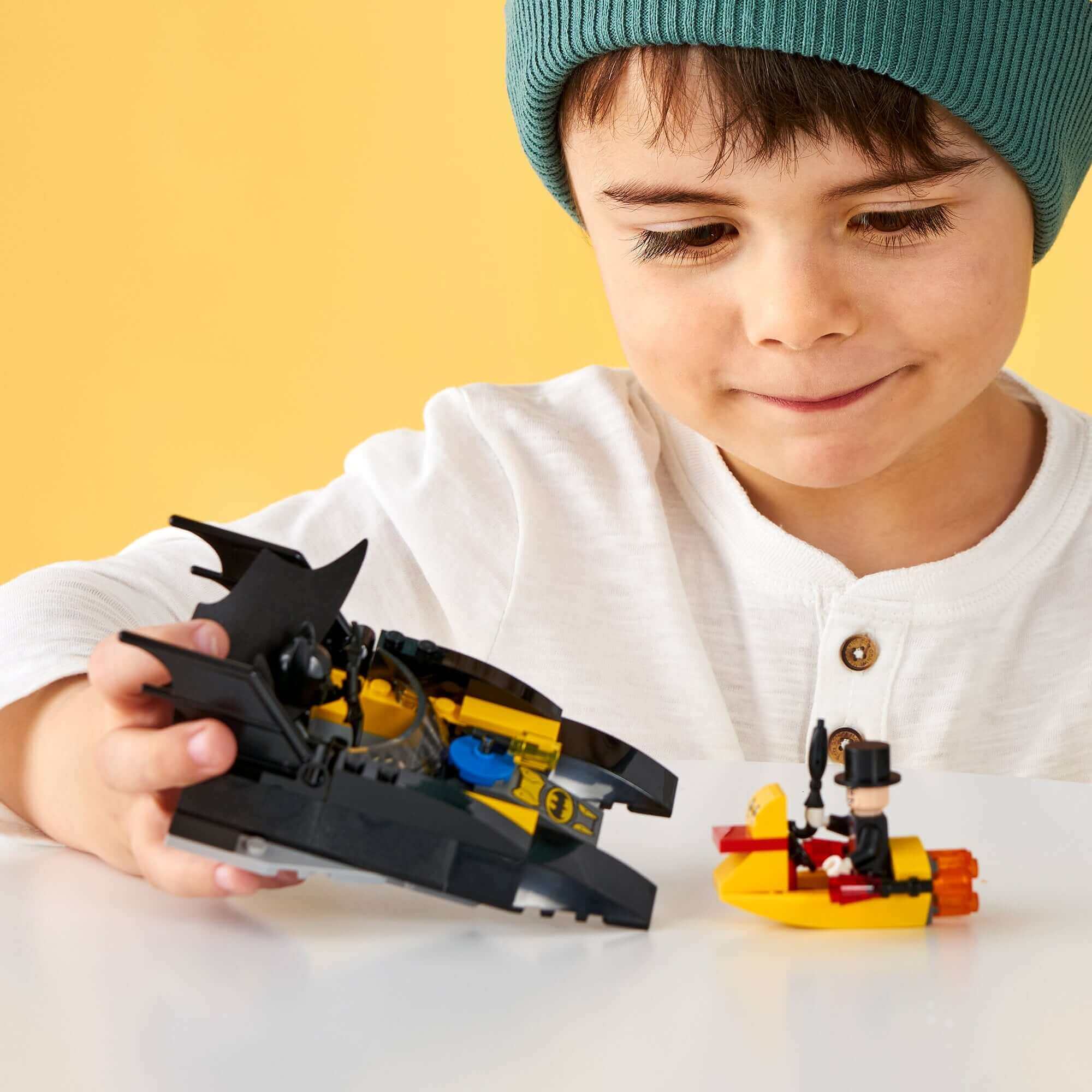 Child playing with LEGO® Batman Batboat and The Penguin minifigure, enjoying superhero adventures.