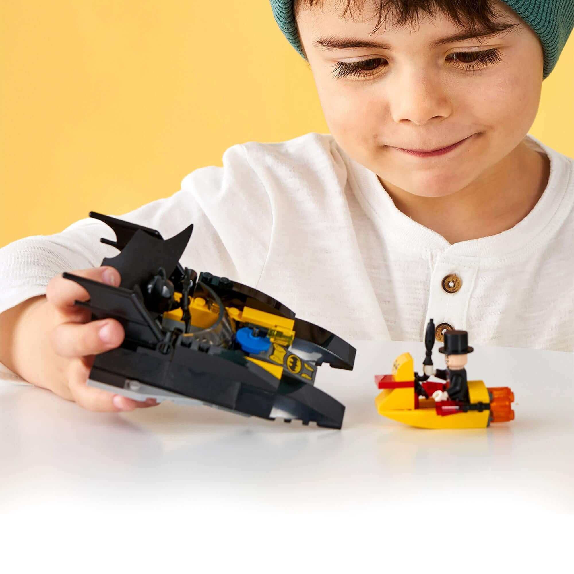 Child playing with LEGO® Batman Batboat and Penguin minifigure in a bright setting, enjoying hands-on superhero fun.