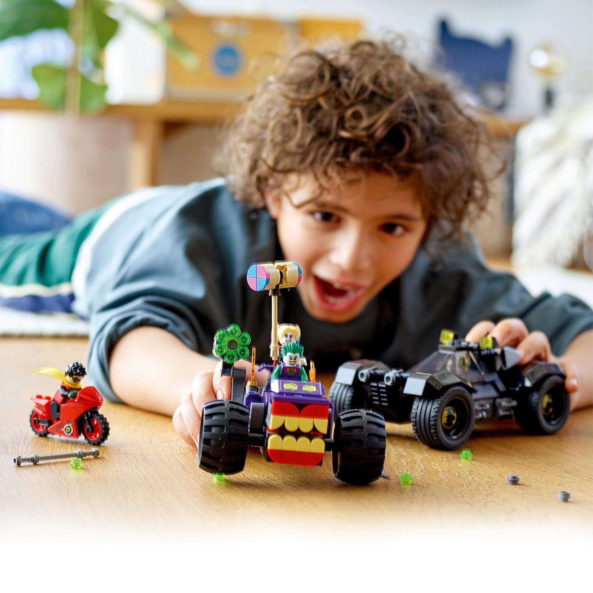 Child playing with LEGO® DC Batman Joker's Trike Chase set featuring characters and vehicles on the floor.