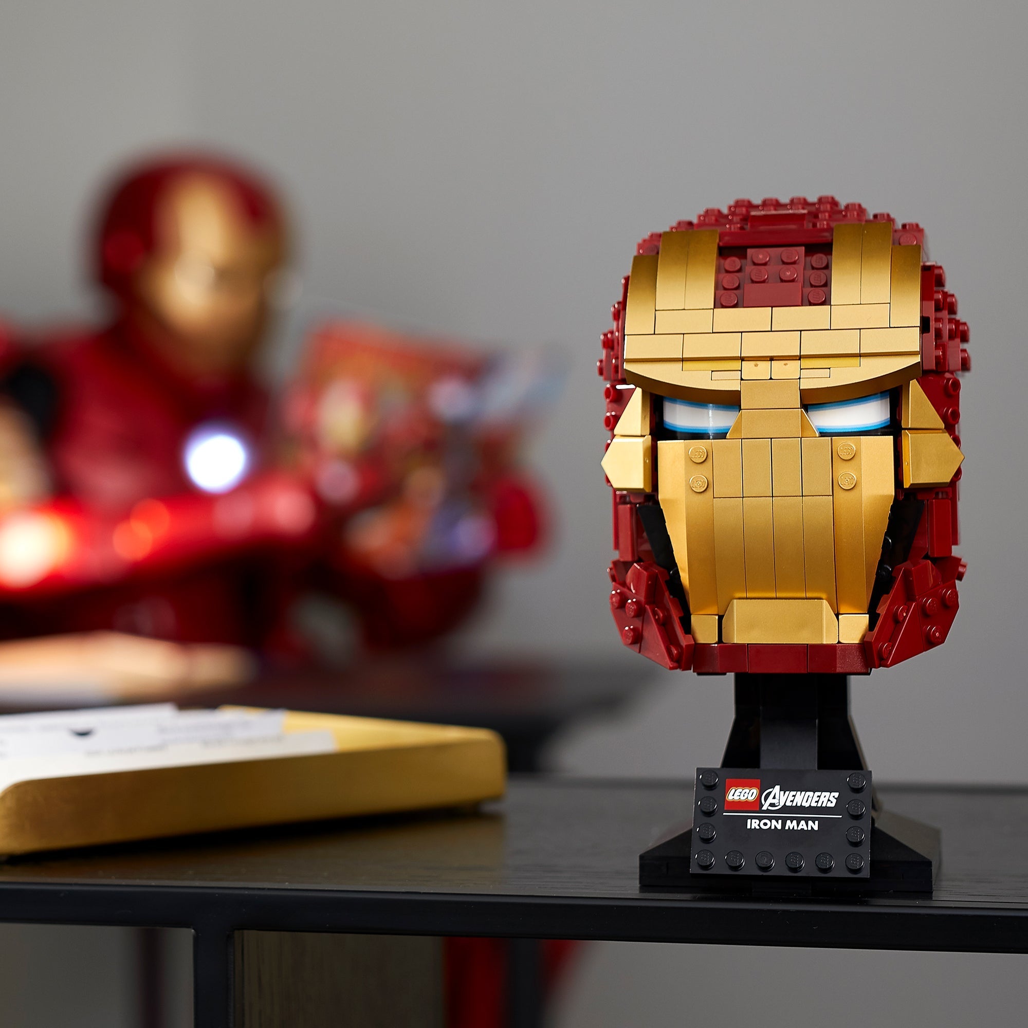 LEGO® Marvel Iron Man Helmet 76165 displayed on a shelf with Iron Man figure in background, showcasing a detailed brick build.