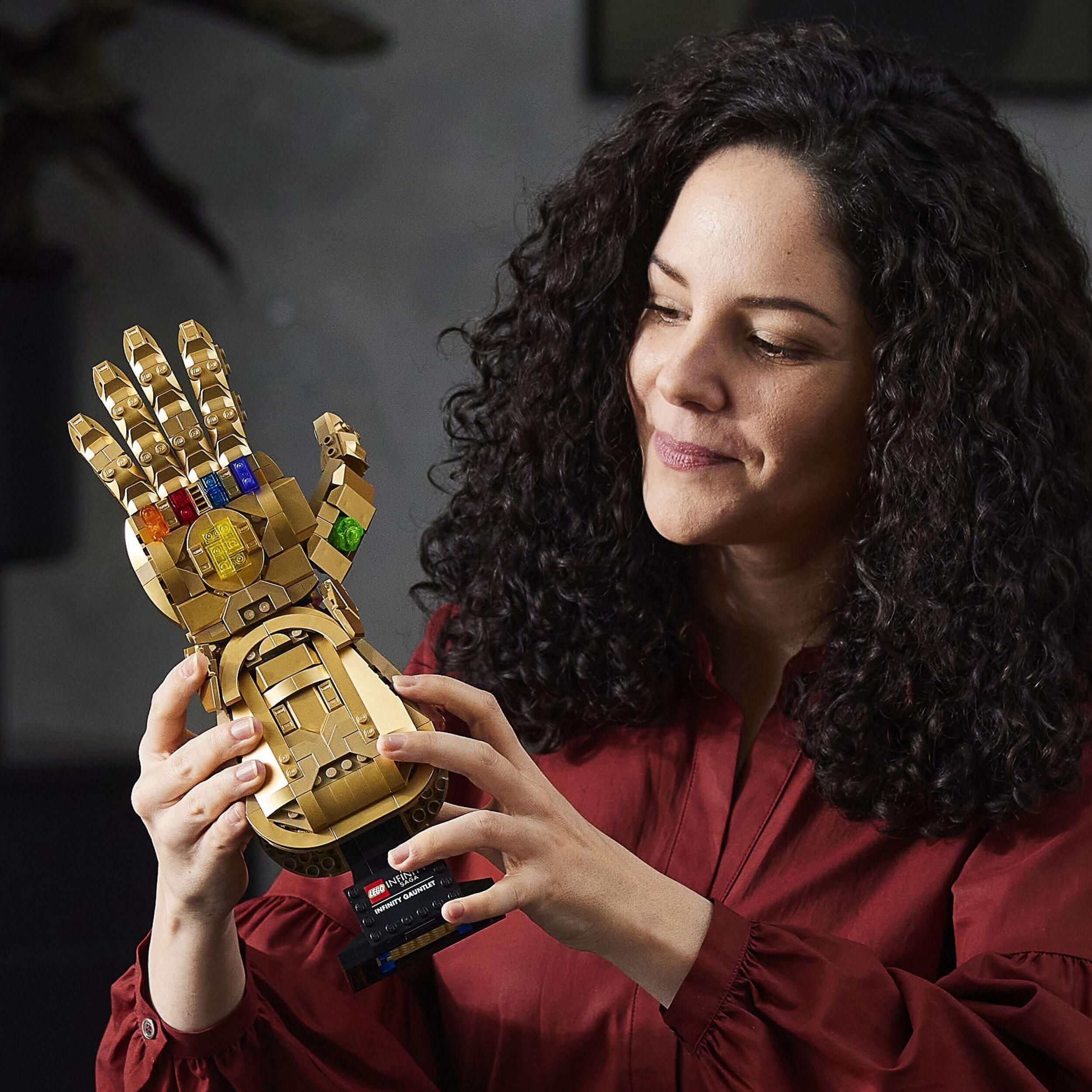 Adult woman marvels at the LEGO® Marvel Infinity Gauntlet set with colorful Infinity Stones and movable fingers.