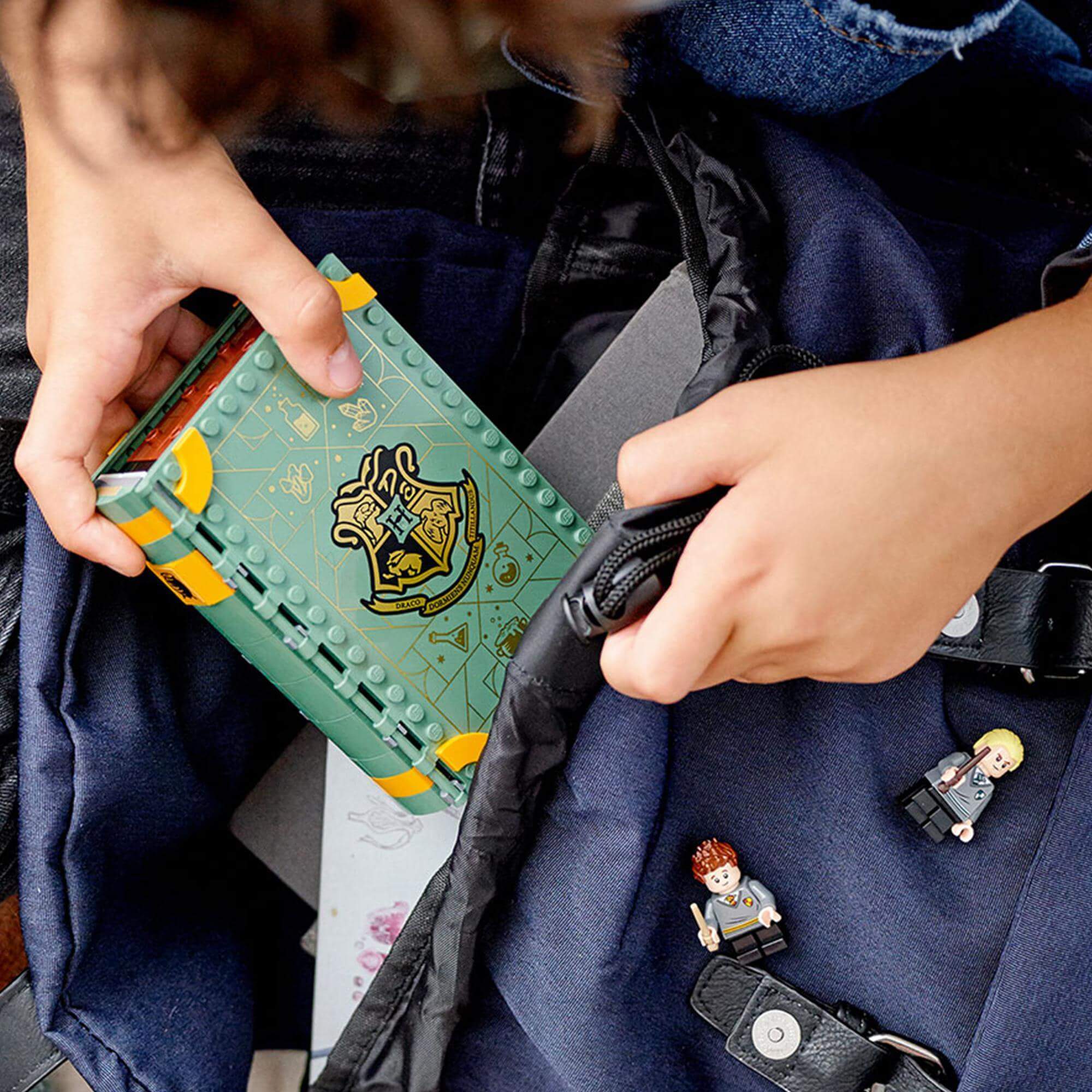 Child's hands holding LEGO Harry Potter Potions Class set with mini figures in a backpack.