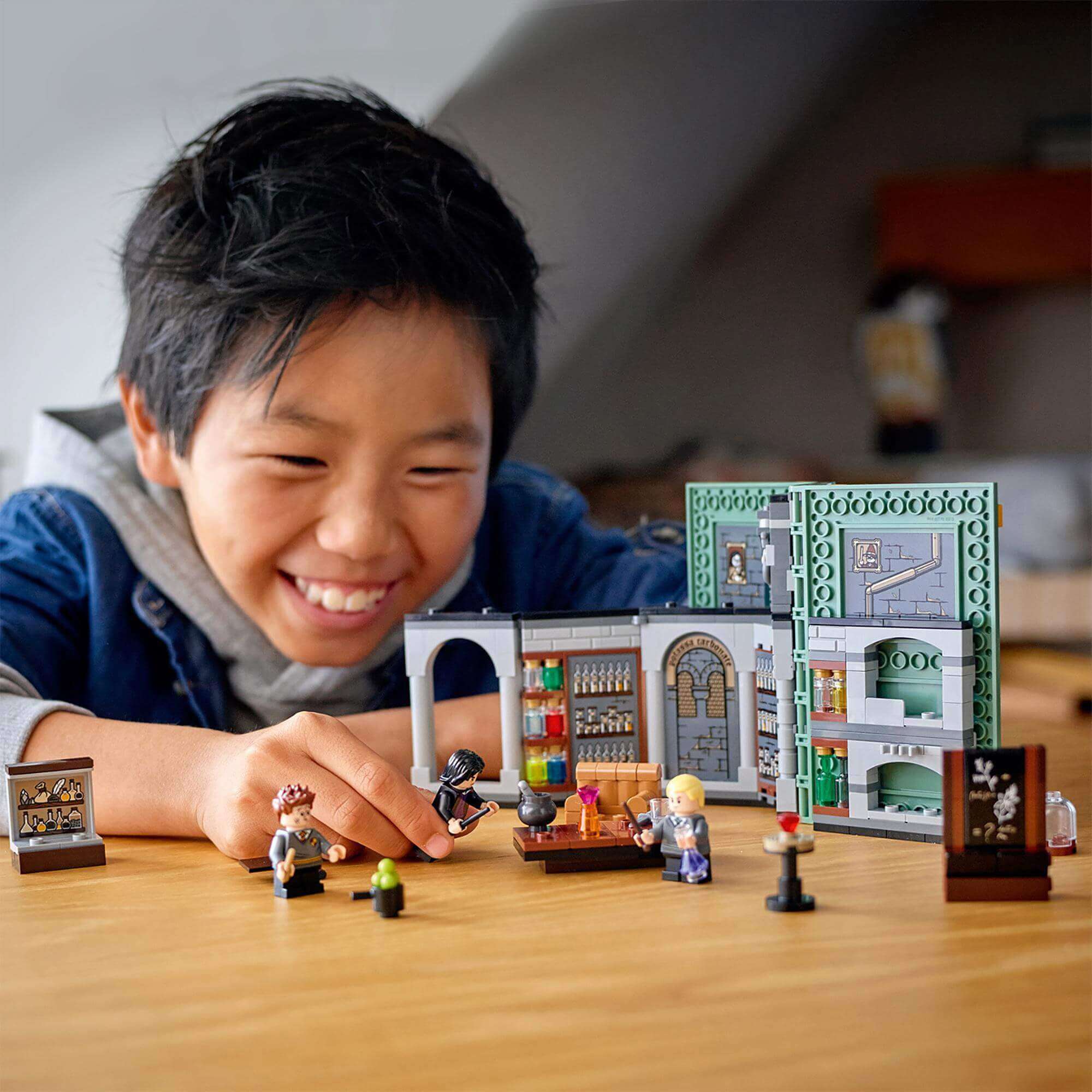 Child joyfully playing with LEGO® Harry Potter Hogwarts Potions Class Set 76383, showcasing magical characters and potion-making.