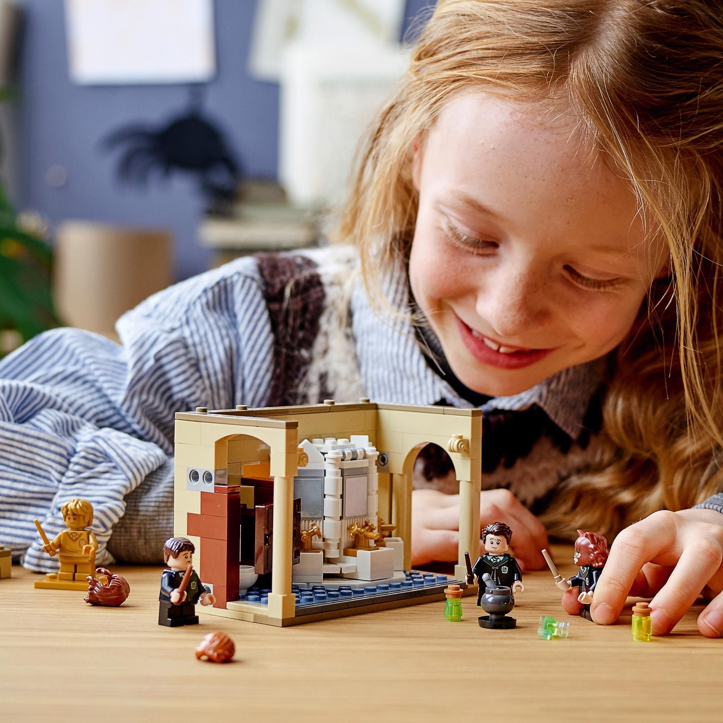 Child playing with LEGO Harry Potter 76386 set, featuring Hogwarts bathroom and character figures.