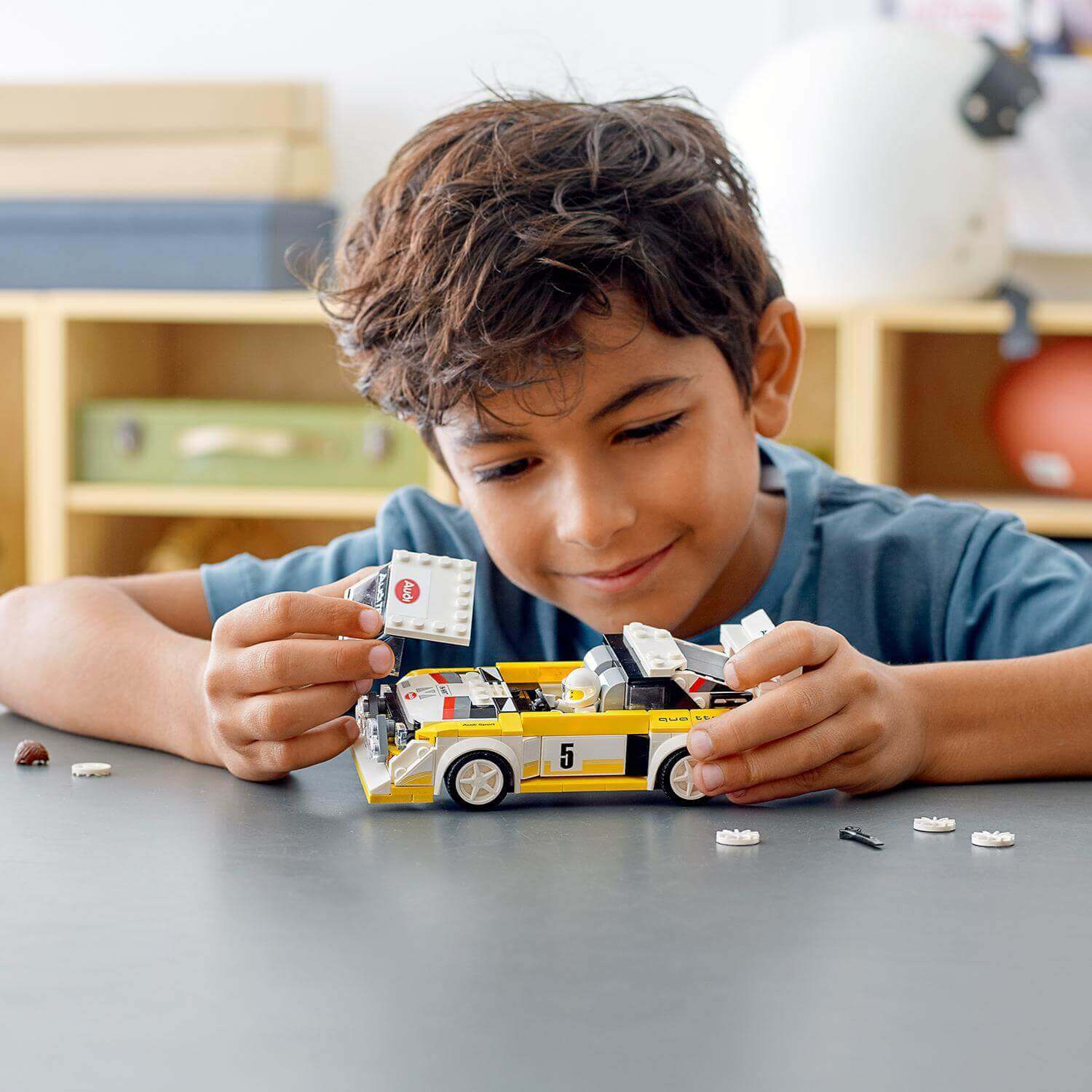 Boy building and displaying a LEGO® Speed Champions Audi Sport Quattro S1 model car with accessories.