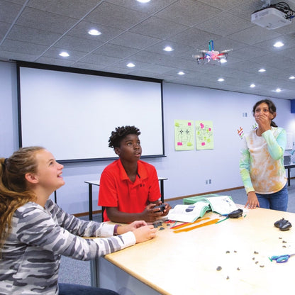 Students engaged in a STEM lesson, working with a flying drone in a classroom environment.