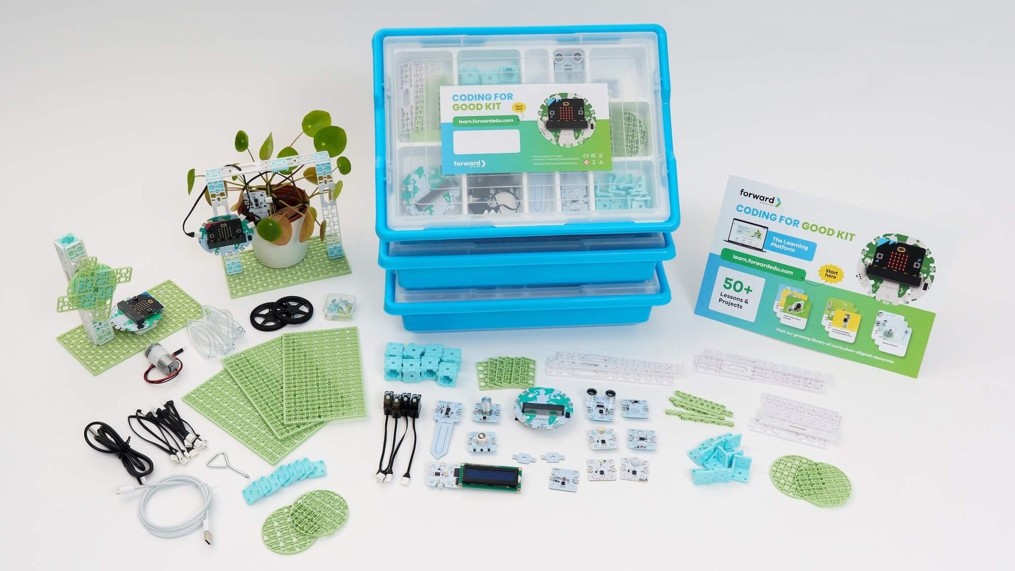 An overhead shot of the Coding for Good Kit contents, featuring a stack of blue storage bins, various sensors, modular building blocks, a micro:bit interface, and a built prototype interacting with a potted plant.