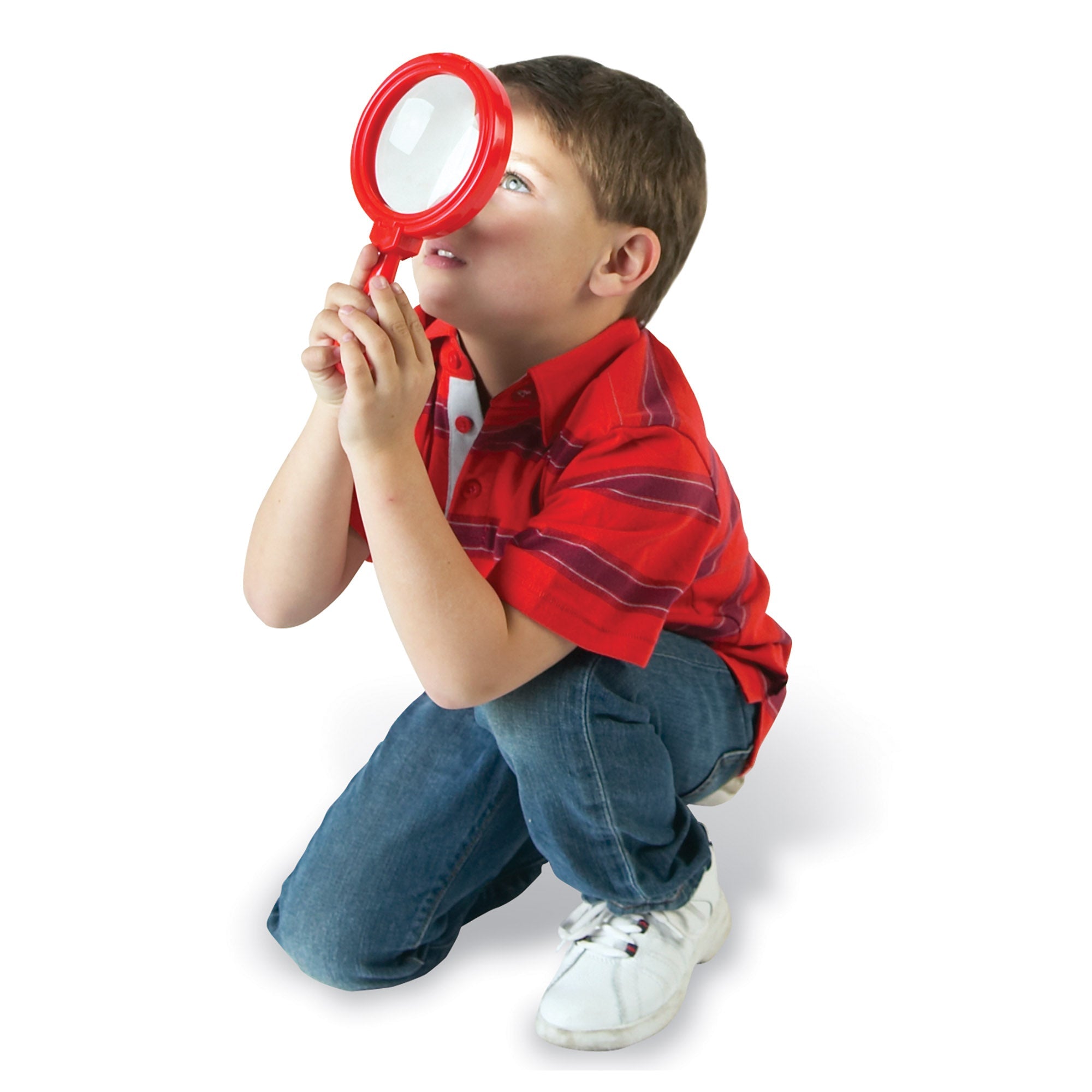 A full-length studio shot against a white background of a young boy crouching down in a red striped shirt and jeans. He is intently looking upward through a large, red Learning Resources Jumbo Magnifier held with both hands, focusing on an unseen object above. This image demonstrates the child-friendly size and powerful 4.5x magnification of the 20cm tool, showcasing how it engages young learners aged 3+ in natural observation and scientific exploration.