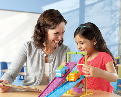 An educator and student smiling while exploring gravity and friction using two toy cars on adjustable purple and blue ramps. Part of a comprehensive STEM activity set for ages 5+.