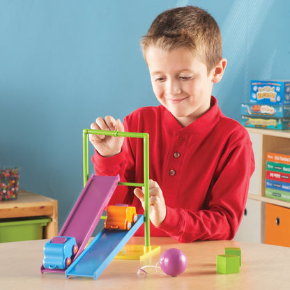 A child in a red shirt experimenting with ramps and toy cars from the Simple Machines set. The scene highlights early engineering and problem-solving investigations.