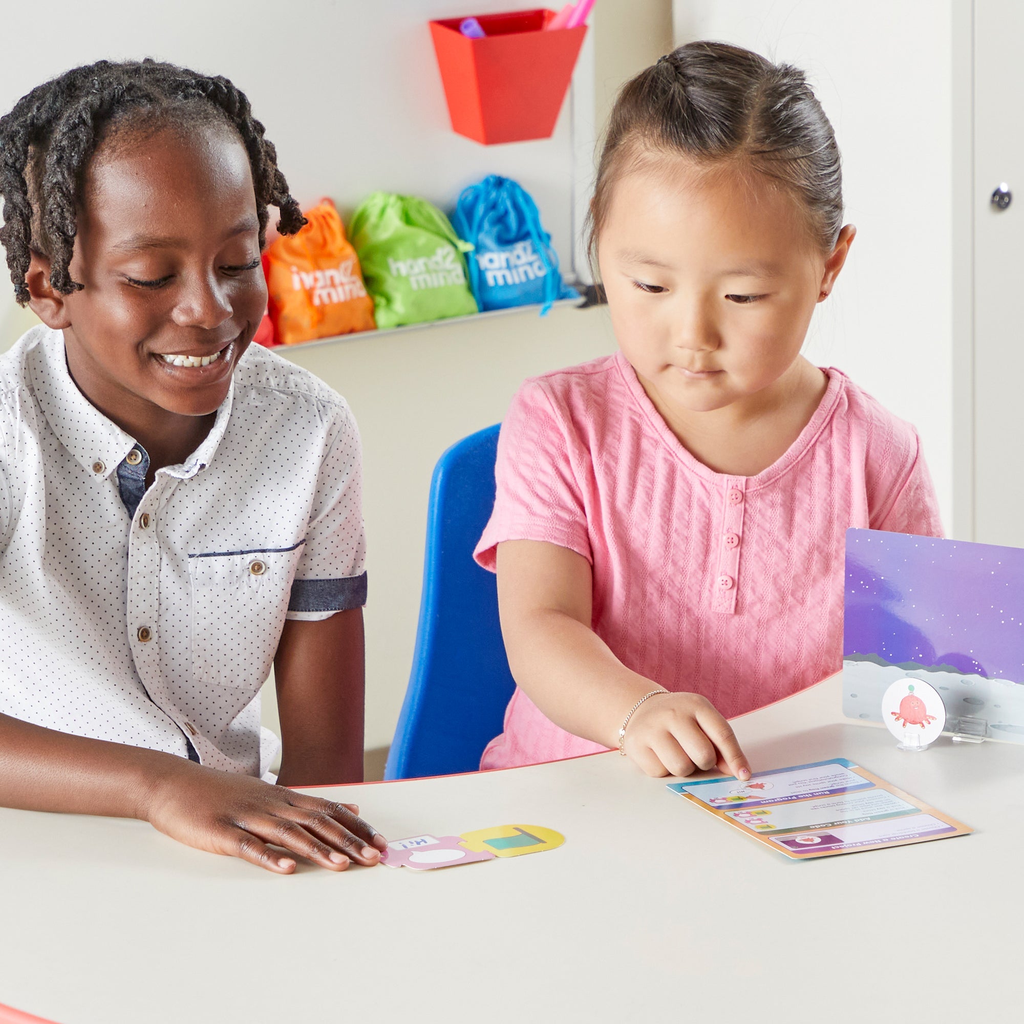 A studio shot of the ScratchJr Block-Based Coding Student Activity Set on a white background. It includes colourful coding tiles, character sprites with stands, backdrop cards, and an activity guide.