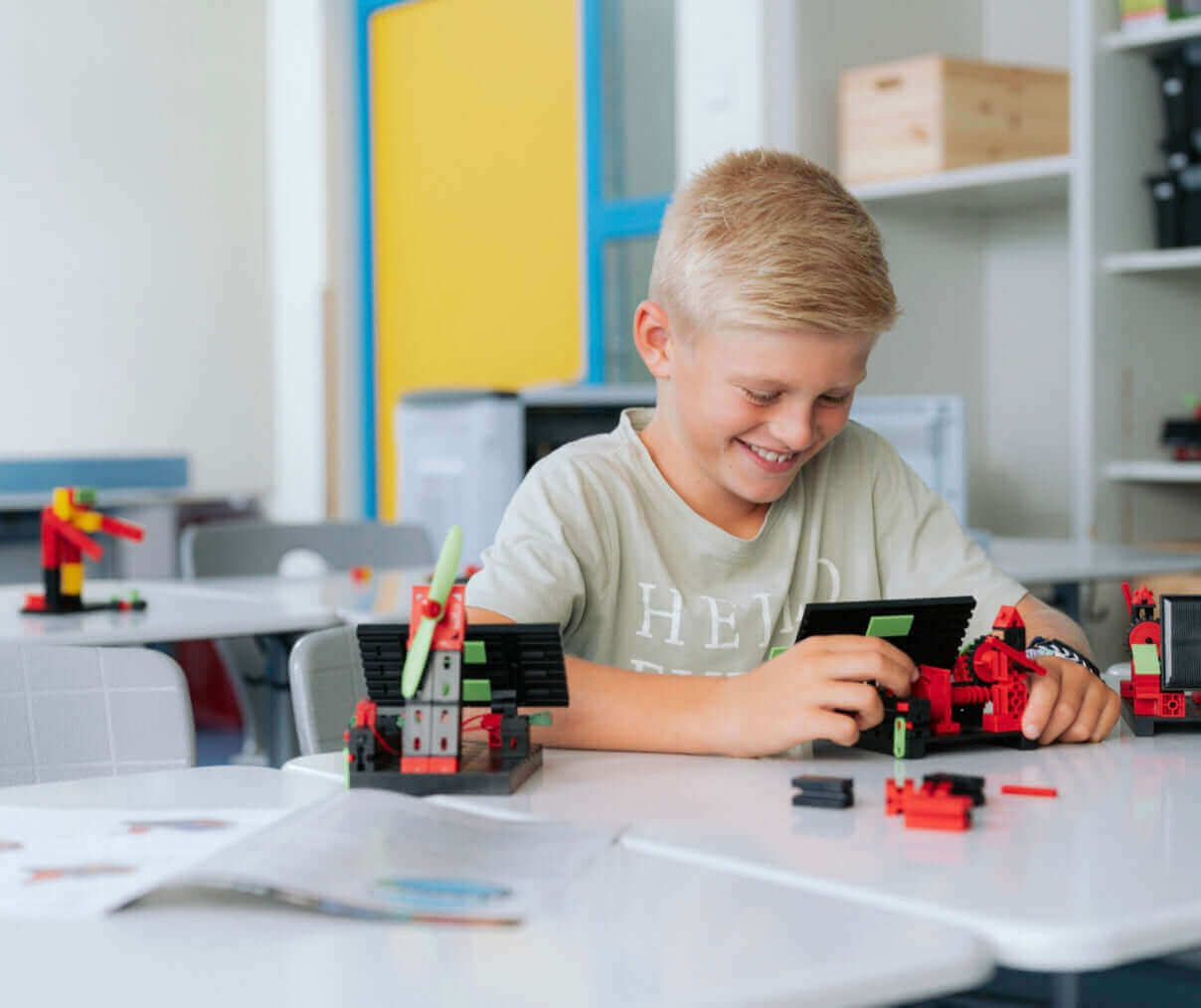 Young boy building with colorful construction toys in a bright classroom, smiling while engaged in creative play.