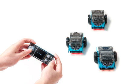 Hands controlling three Makeblock mBot 2 robots with a smartphone, showcasing educational robotics.