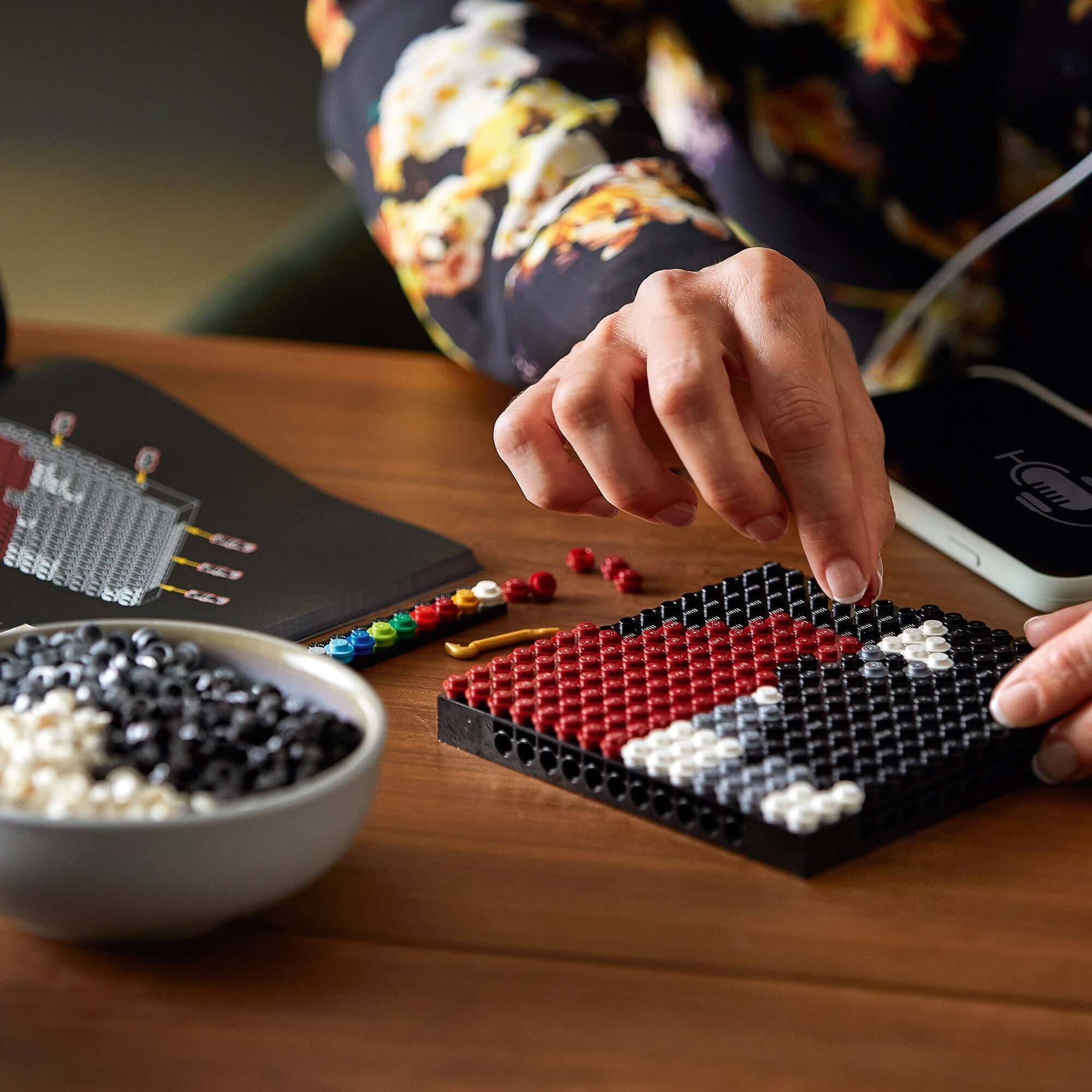 Close-up of a person assembling LEGO® Art Harry Potter Hogwarts Crests set, focused on colorful beads and a black baseplate.