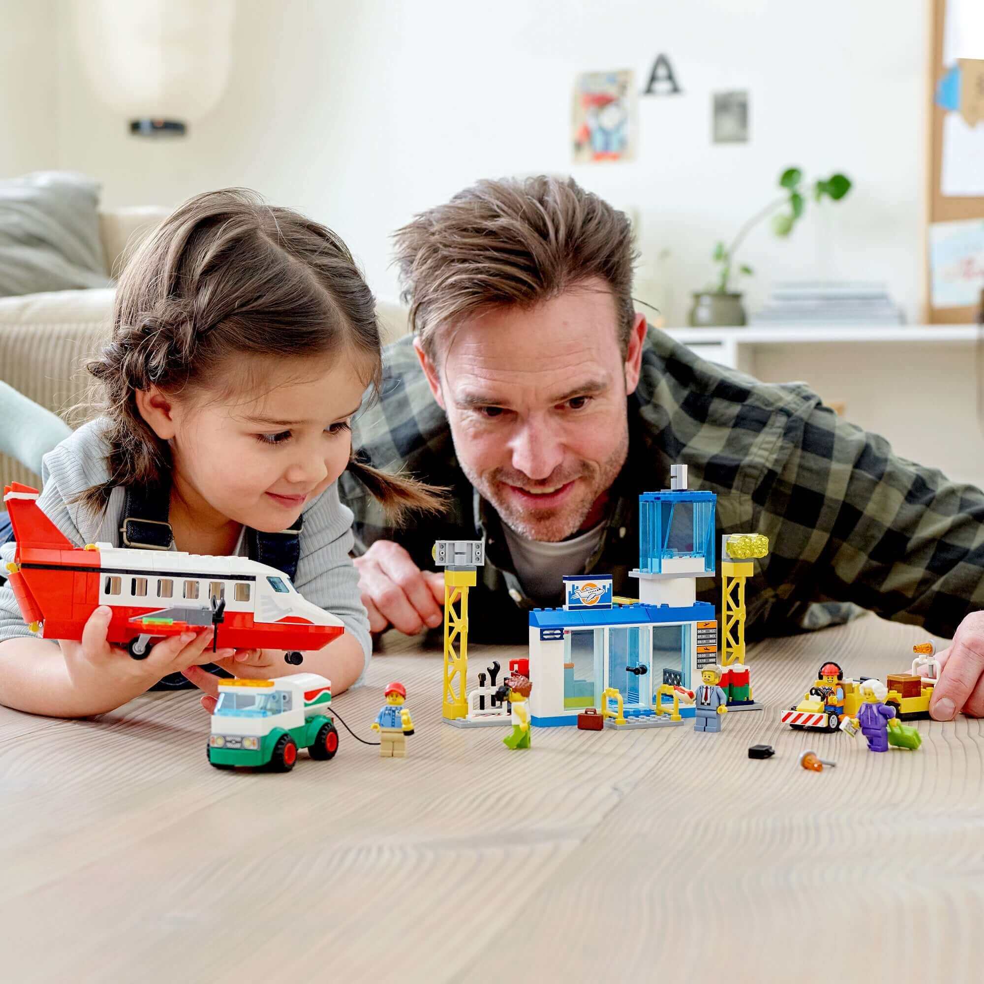 Father and daughter playing with LEGO® City 4+ Central Airport set, featuring a charter plane, terminal, and minifigures.