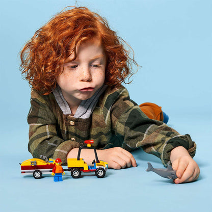 Child playing with LEGO® City Beach Rescue ATV set, featuring lifeguard and water scooter near a toy shark.