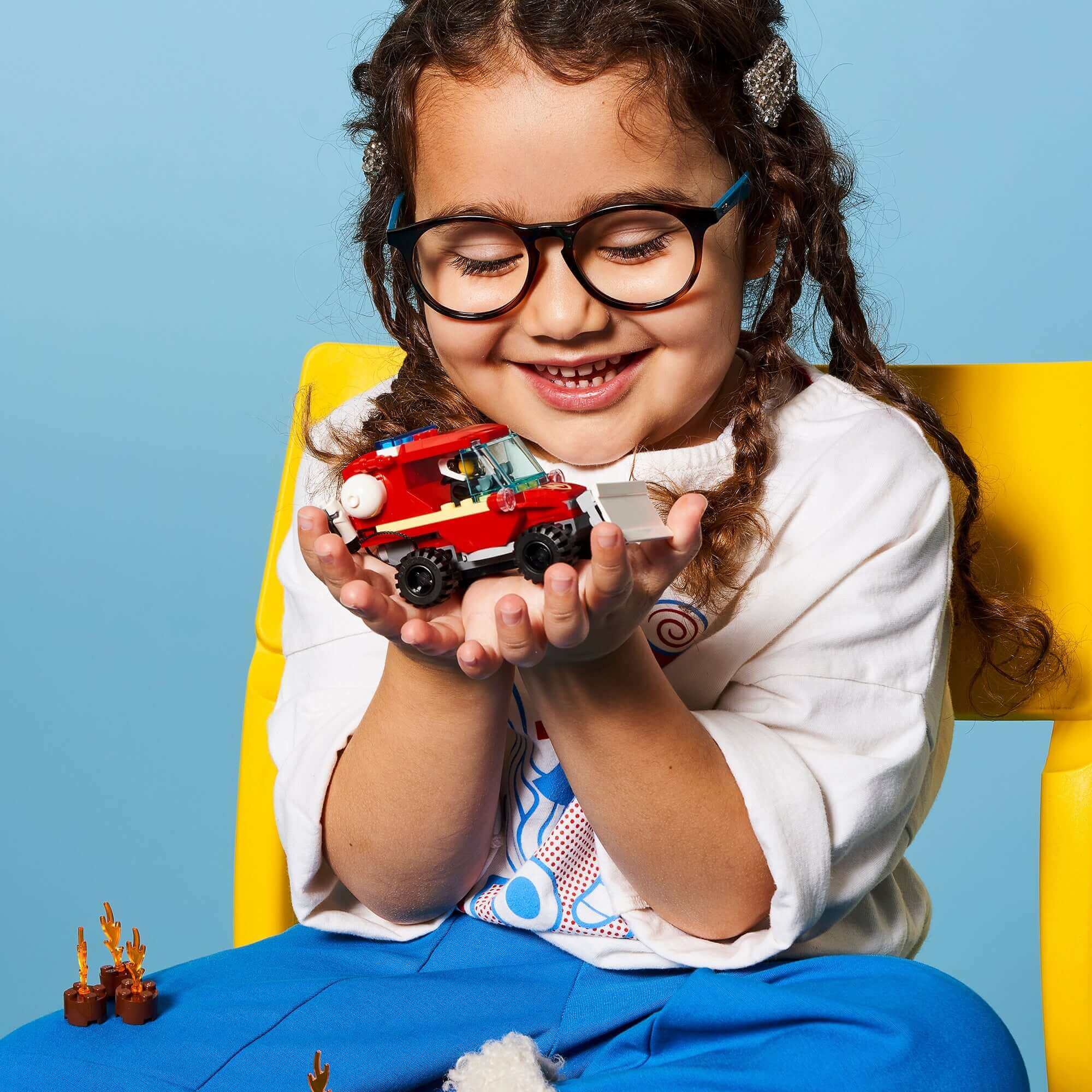 Child holding LEGO® City Fire Hazard Truck 60279, smiling while enjoying pretend play with the fire truck toy.
