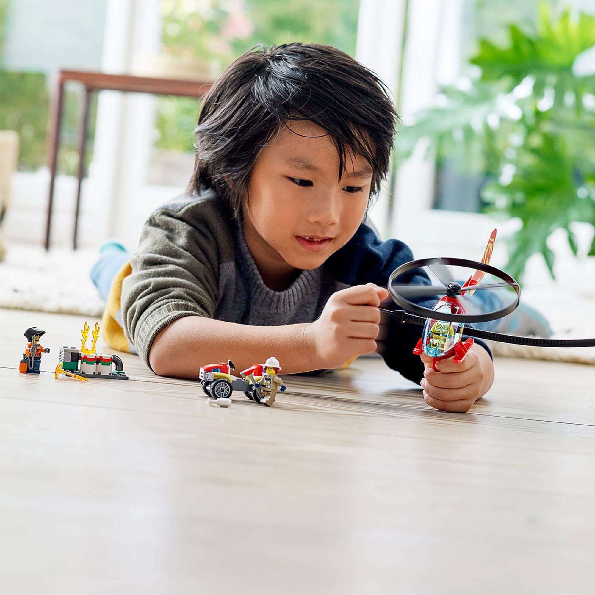 Child playing with LEGO® City Fire Helicopter Response Set 60248, featuring helicopter and rescue figures on the floor.