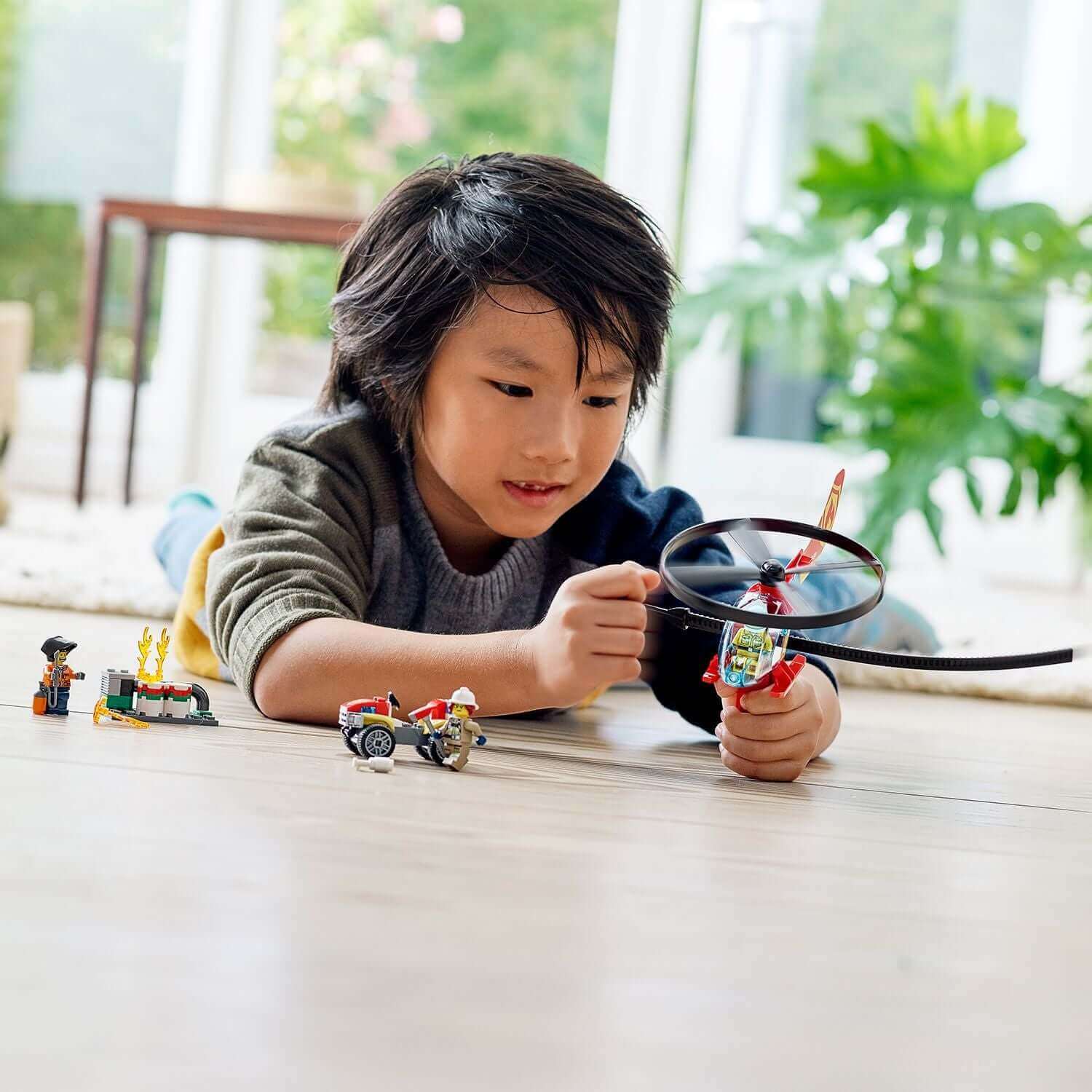 Child playing with LEGO® City Fire Helicopter Response Set 60248, featuring helicopter and minifigures on a floor.