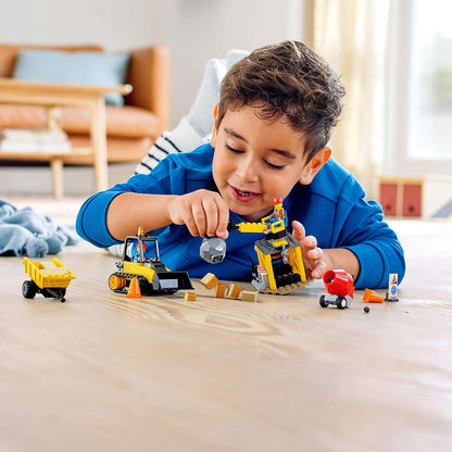 Child playing with LEGO® City Great Vehicles Construction Bulldozer set, including vehicles and worker minifigures.