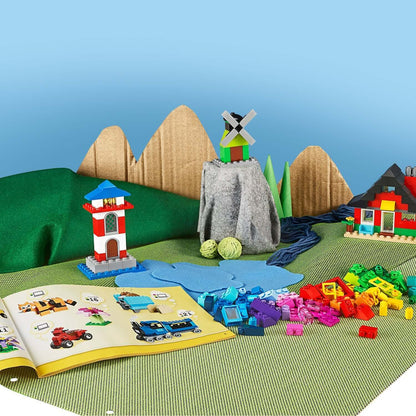 Colorful LEGO® Classic 4+ Bricks and Houses Set 11008 with built structures and instruction book on a playful landscape.