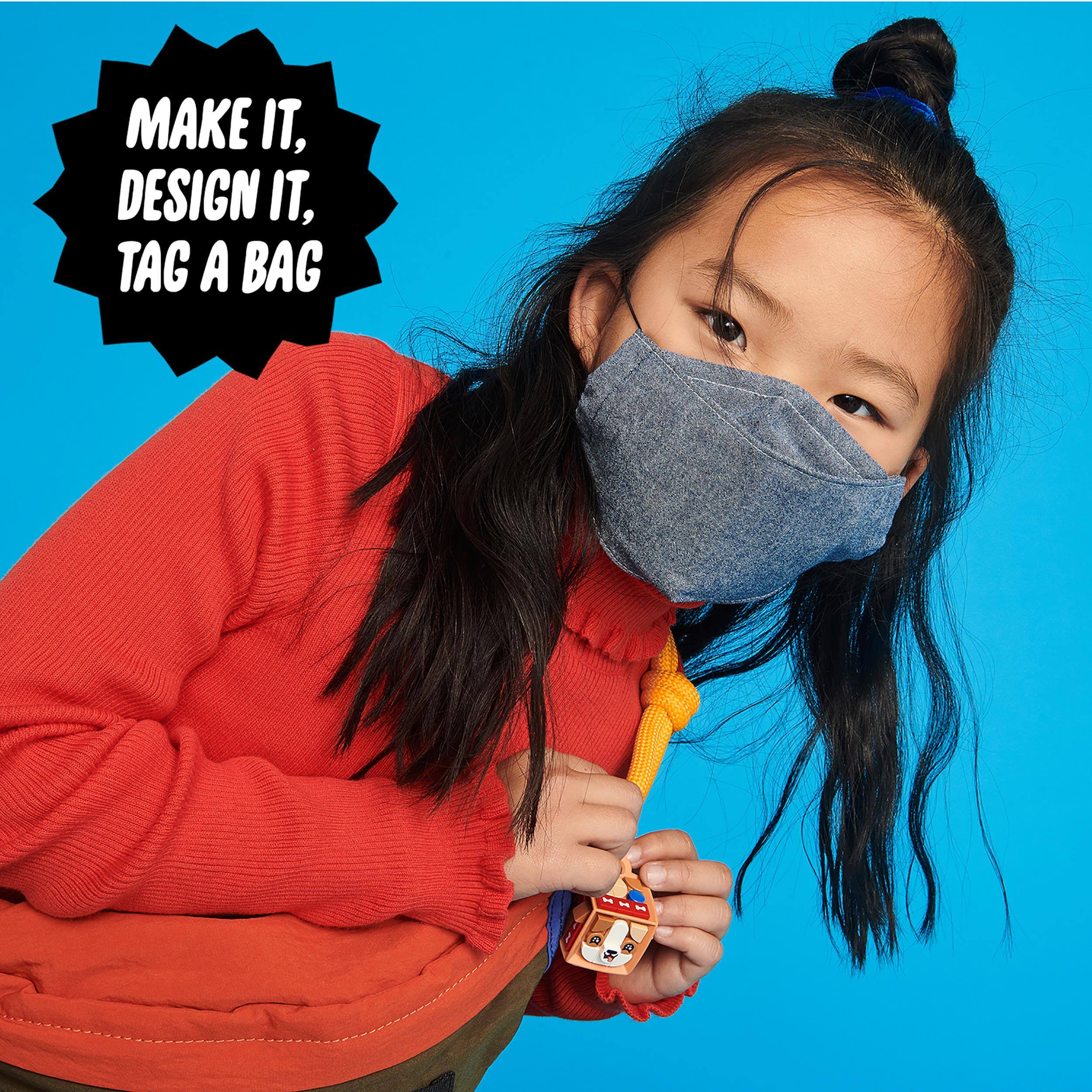 Child wearing a mask, holding a colorful bag tag from the LEGO® DOTS craft set against a vibrant blue background.