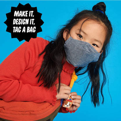 Child wearing a mask, holding a colorful bag tag from the LEGO® DOTS craft set against a vibrant blue background.