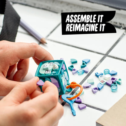 Child assembling LEGO® DOTS Bag Tag Narwhal craft kit with colorful tiles on a table.
