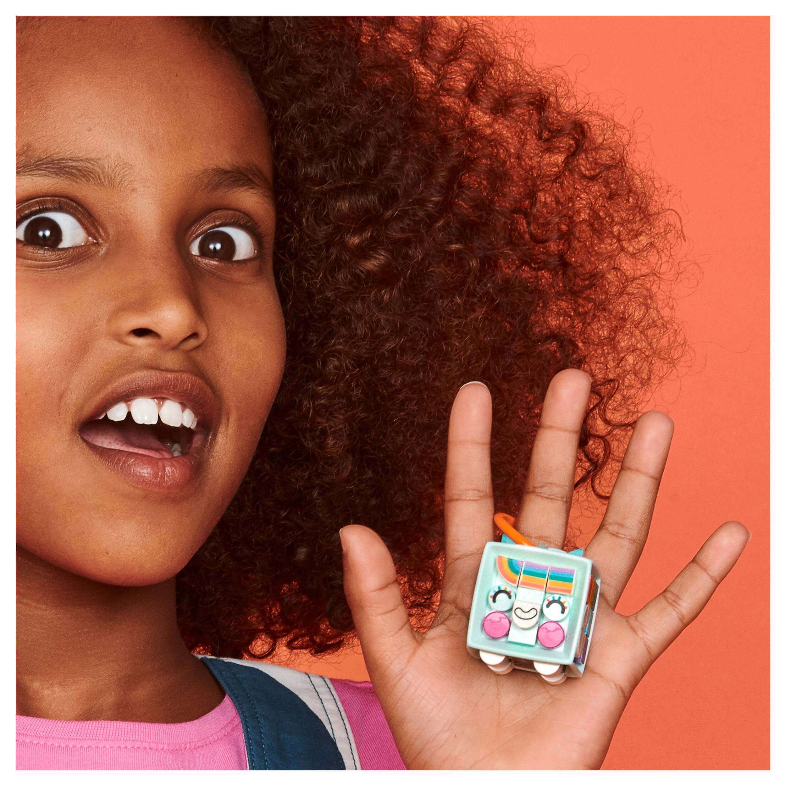 Child showing LEGO® DOTS Unicorn Bag Tag, featuring a colorful design, with a happy expression on her face.
