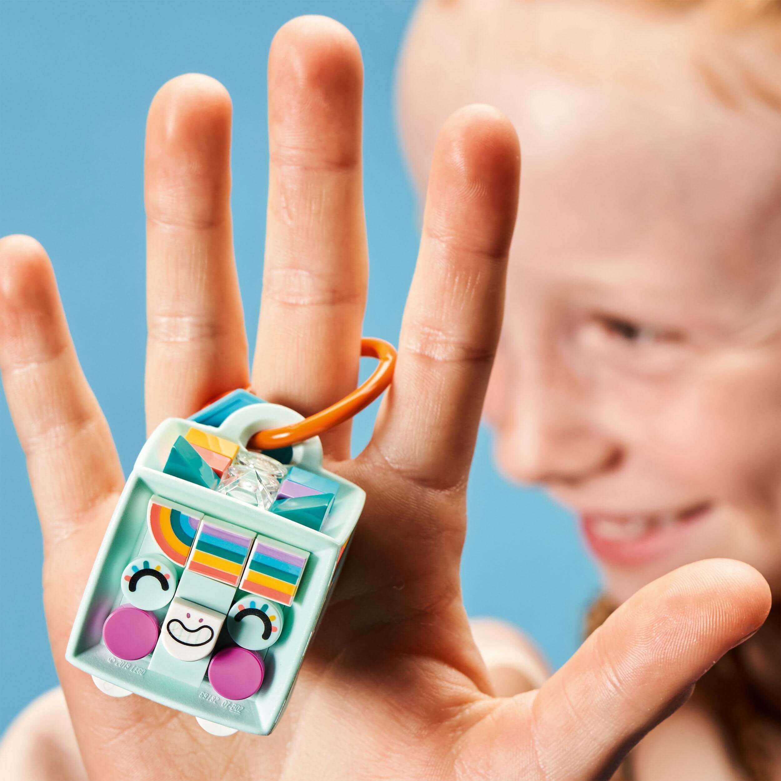 Child holding LEGO® DOTS Bag Tag Unicorn accessory with colorful tiles and mint cube, showcasing creativity.
