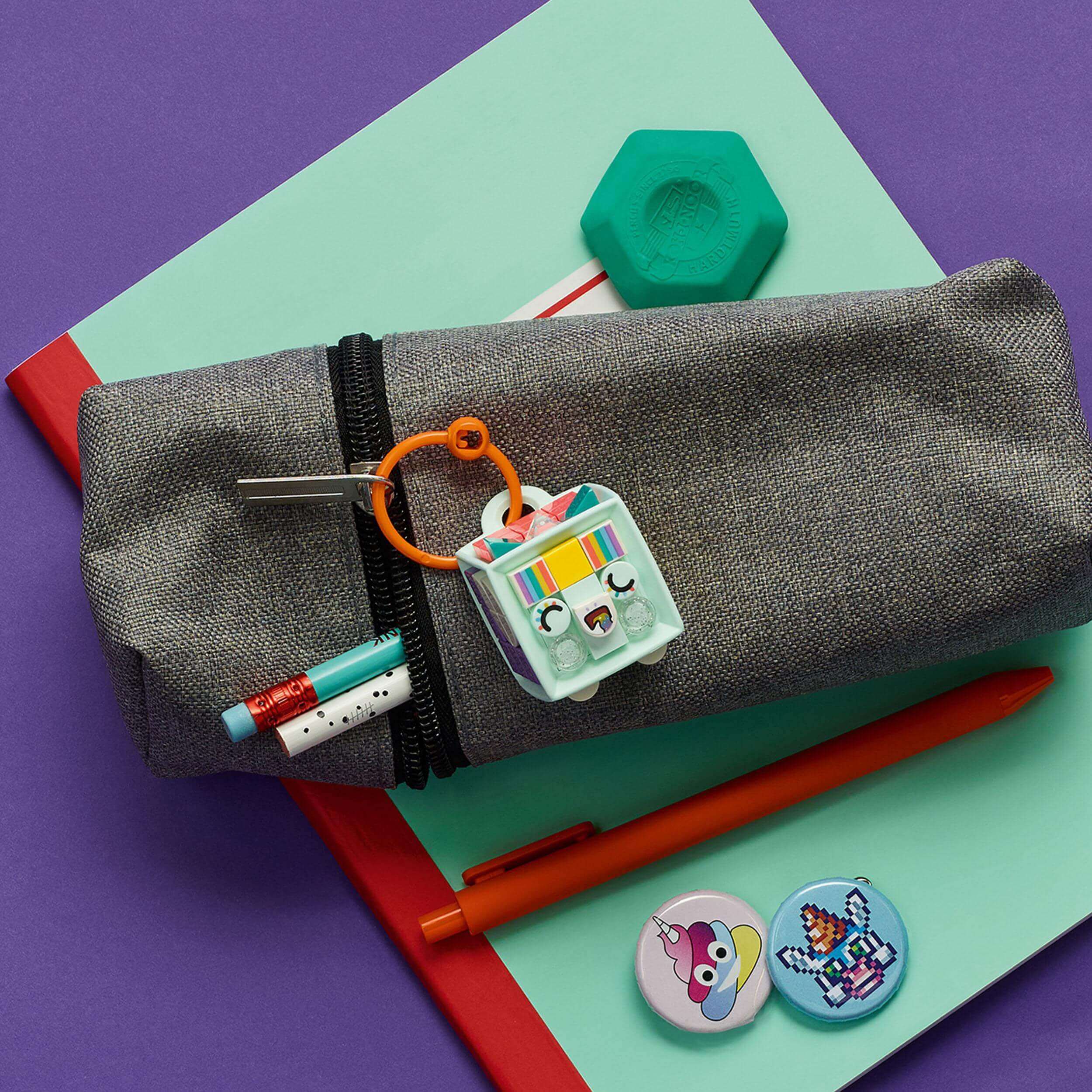 LEGO® DOTS Unicorn Bag Tag kit on a pencil case, surrounded by pens and colorful tiles for creative crafting.
