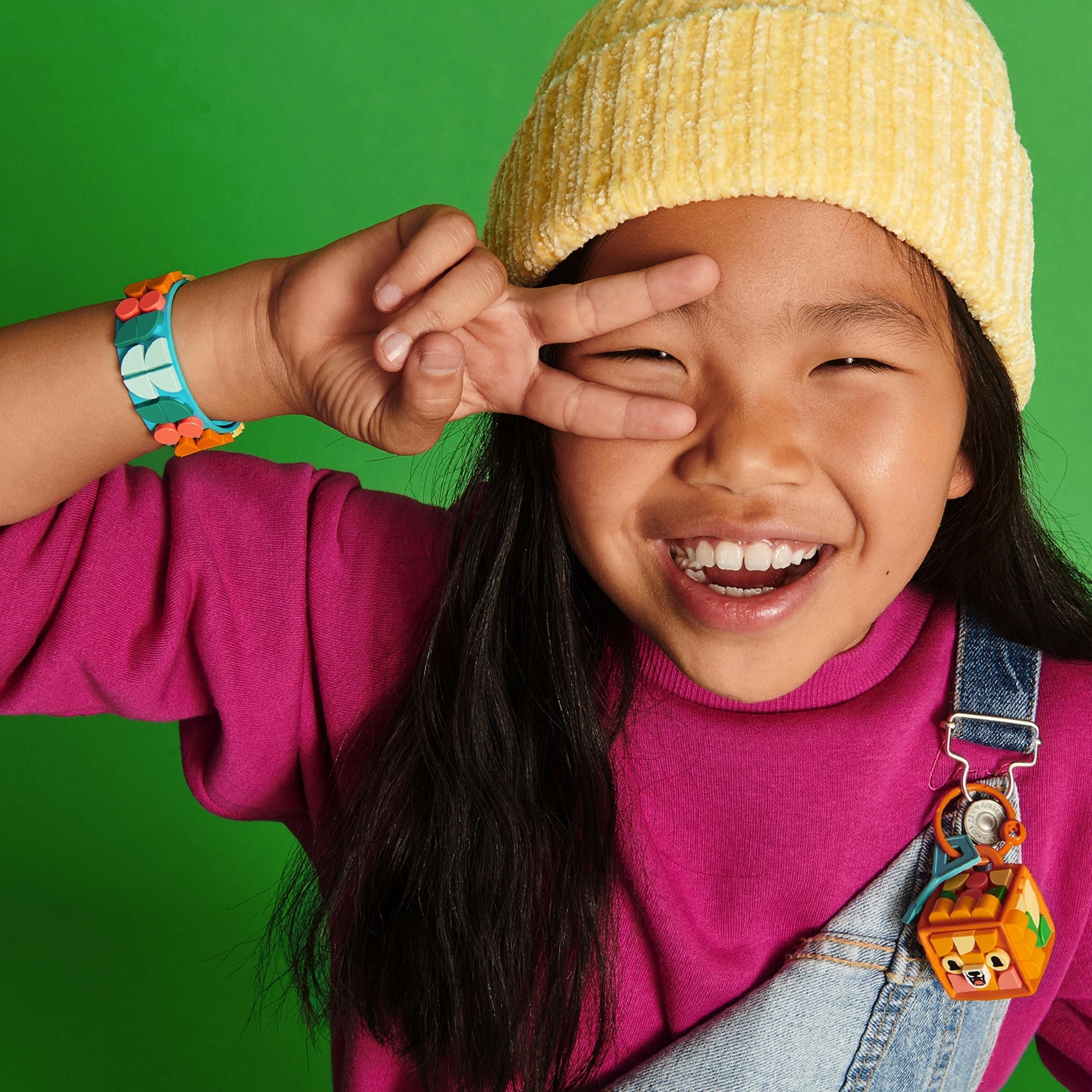 Smiling child wearing a yellow beanie and colorful bracelet, showing creativity with LEGO® DOTS arts and crafts.
