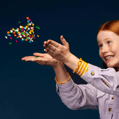 Young girl joyfully tossing colorful LEGO® DOTS tiles into the air, showcasing creativity and fun with craft supplies.