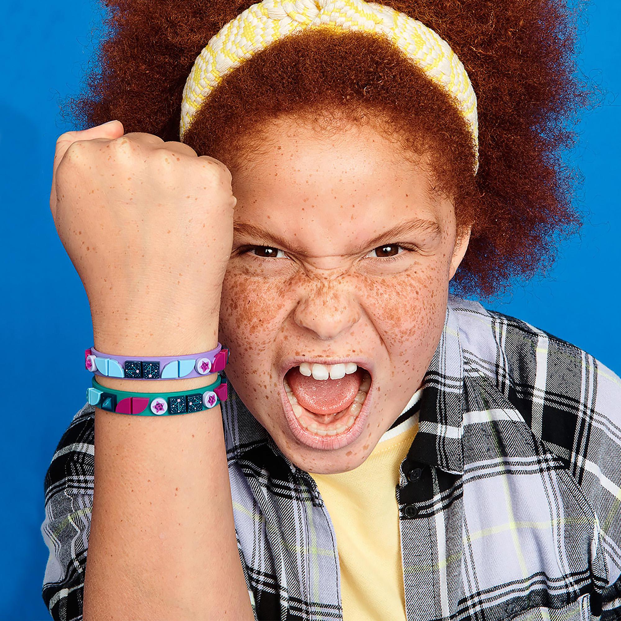 Child showing off LEGO® DOTS Starlight Bracelets in teal and purple with playful enthusiasm.